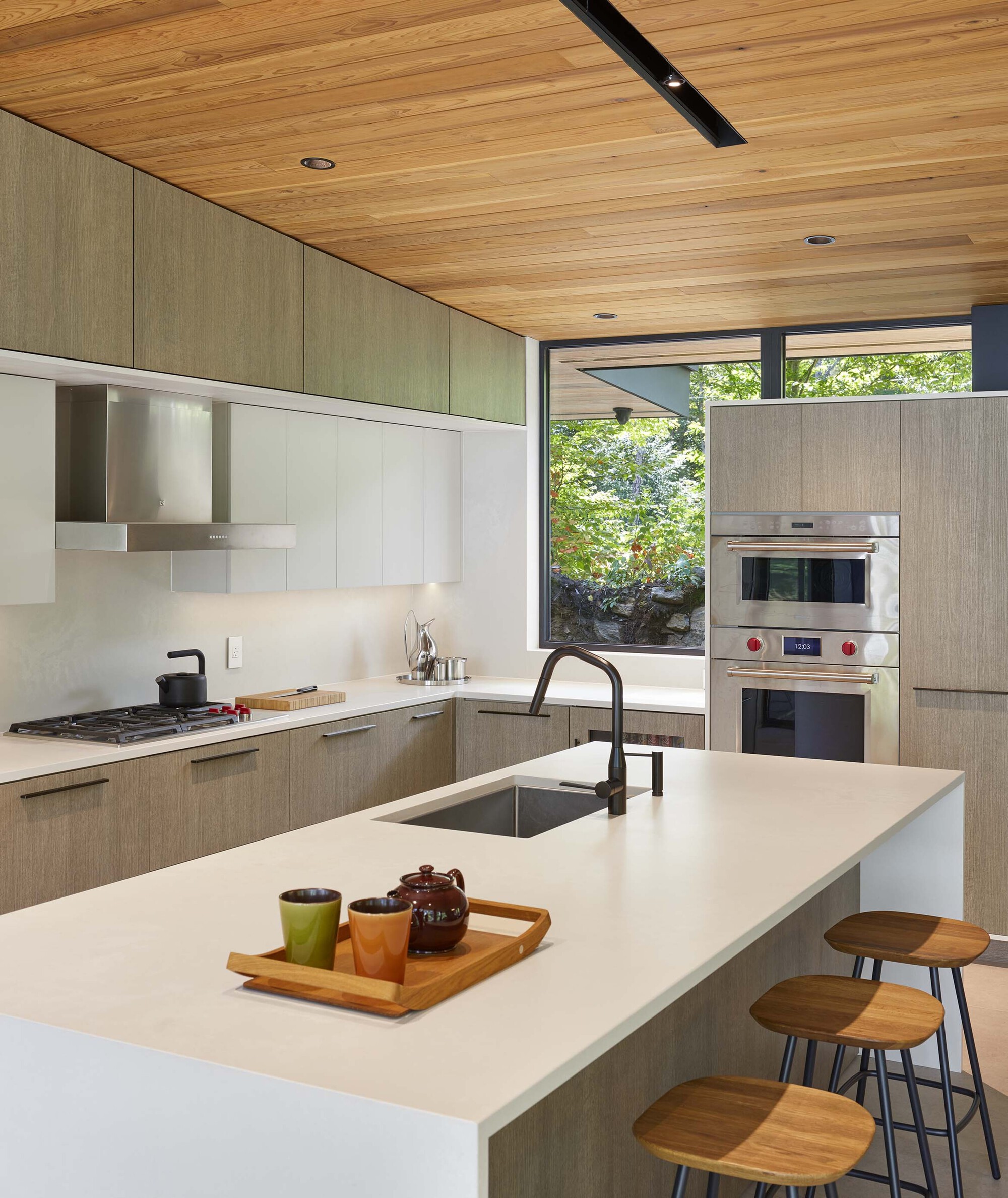 Kitchen island with white countertop and timber cabinetry beneath wood plank ceiling with skylight slot