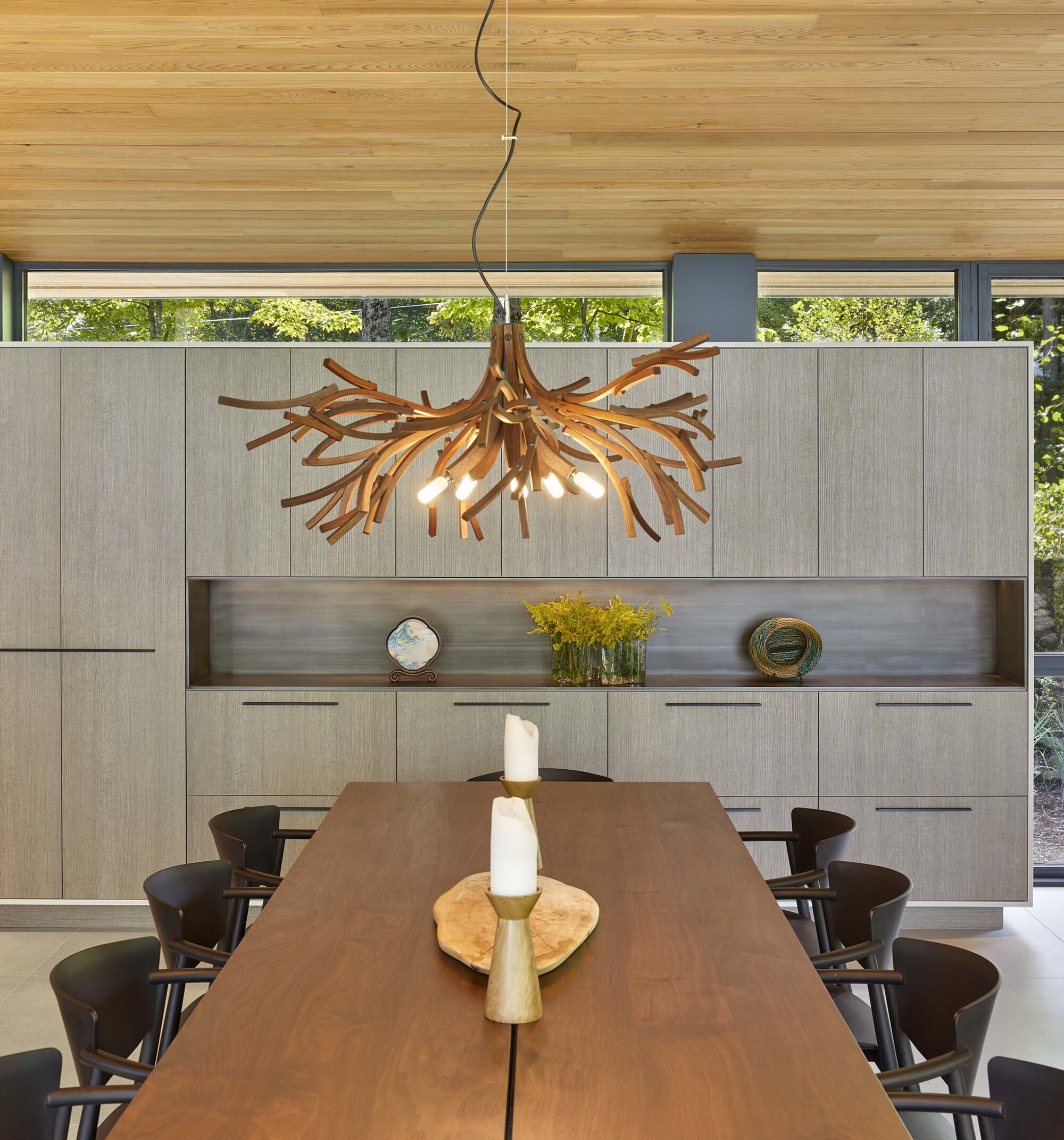 Dining room with sculptural branch chandelier above walnut table and pale grey paneled cabinetry