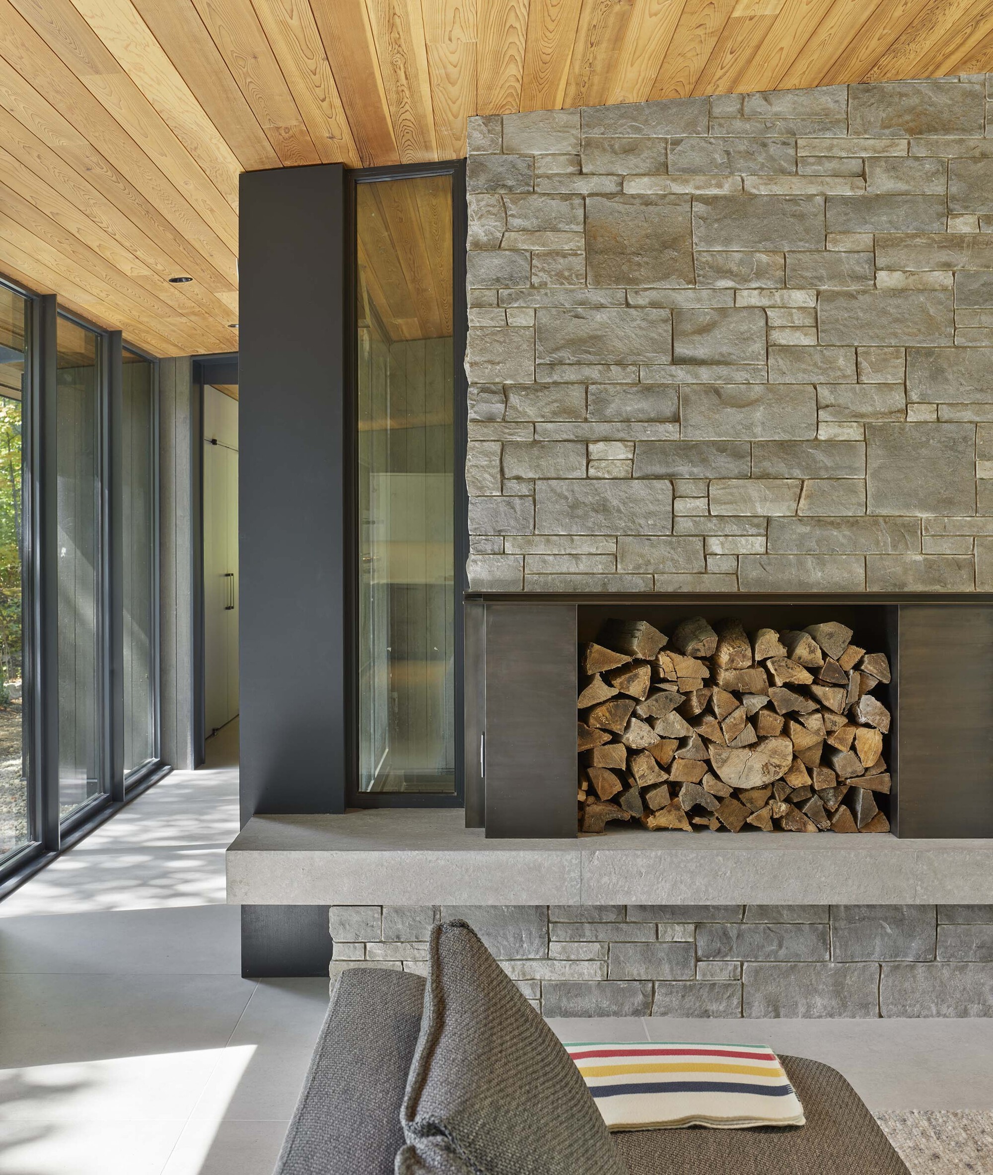 Stacked limestone fireplace with steel-framed firewood niche beneath timber plank ceiling