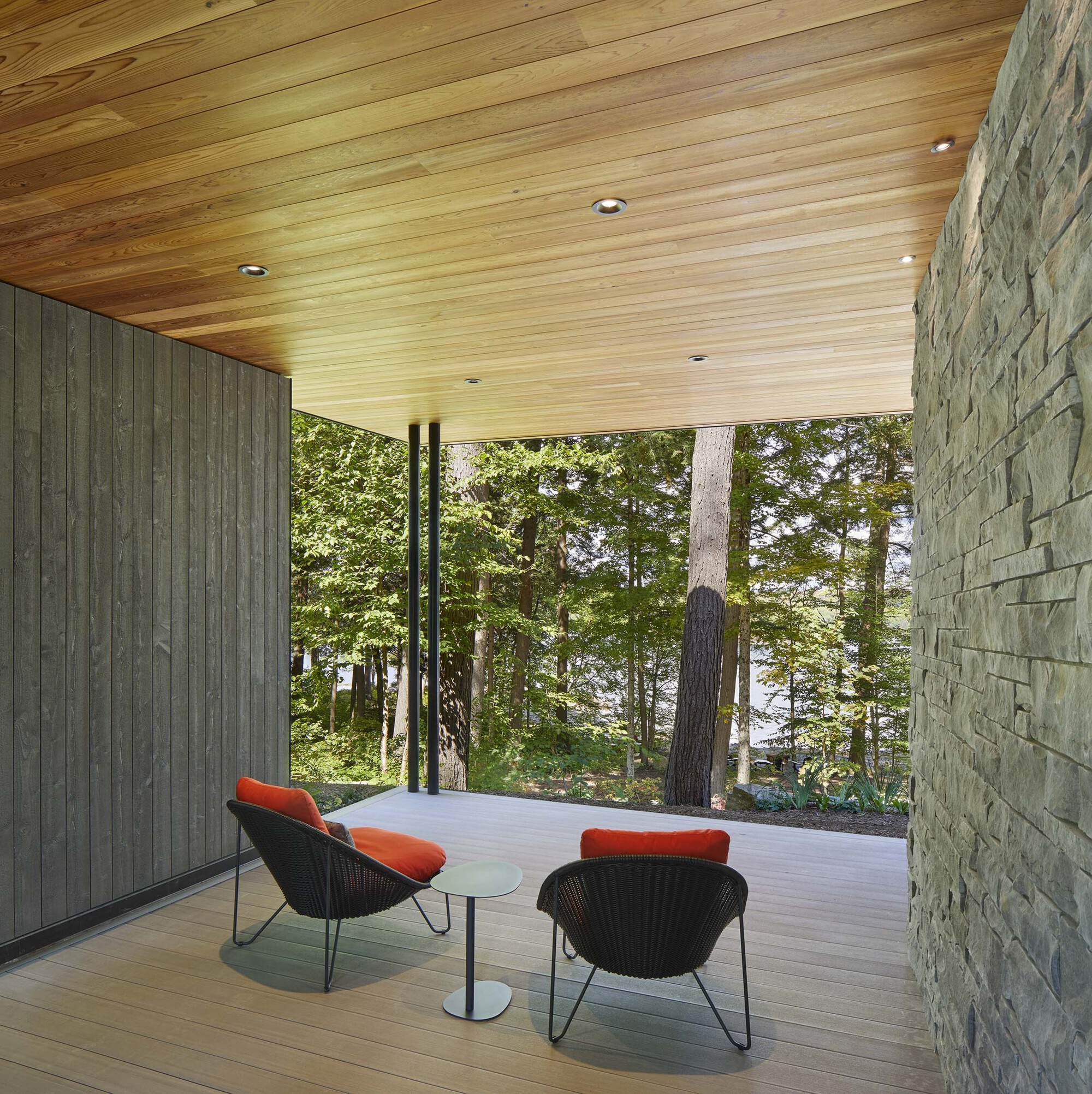 Covered terrace with timber decking and stacked stone wall overlooking forested landscape
