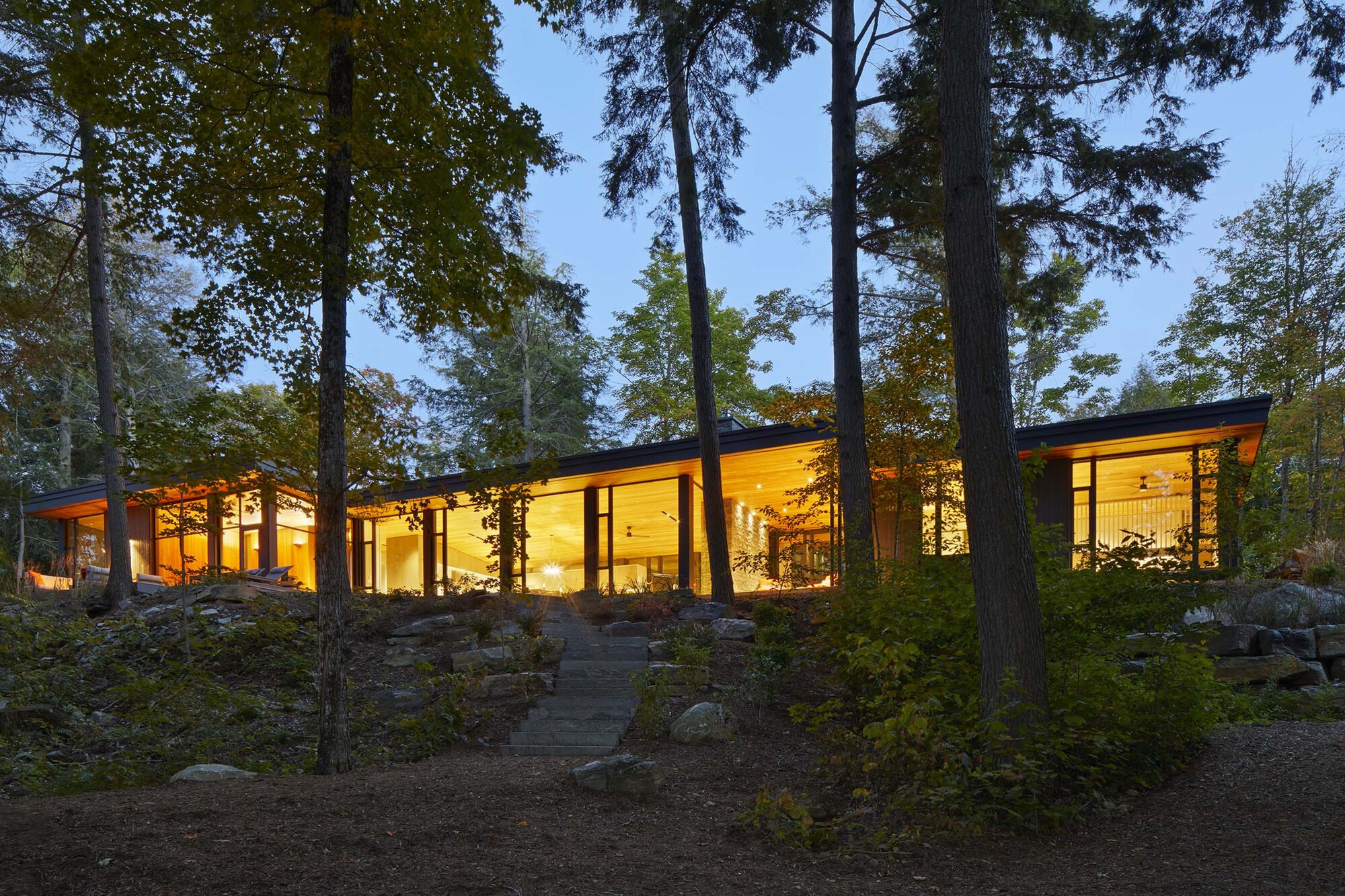 Long glass facade glowing at dusk with steel columns framing views into interior spaces