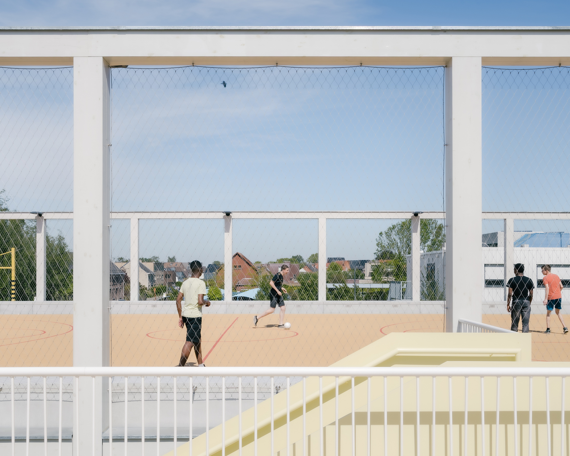 Rooftop sports court framed by white steel columns and mesh netting with players in afternoon light