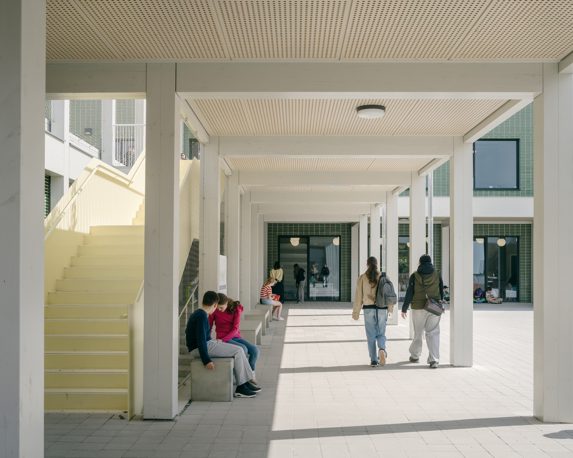 Covered colonnade with timber slat ceiling and concrete bench seating as students gather