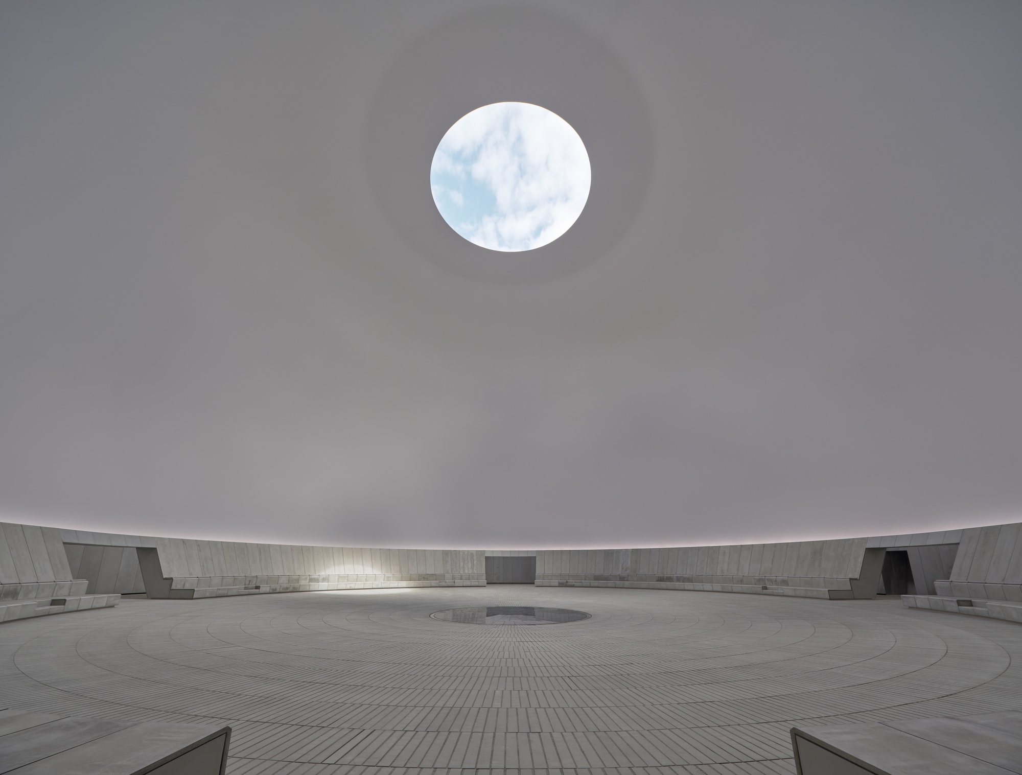 Circular oculus opening in the white domed ceiling above the paved courtyard on an overcast day