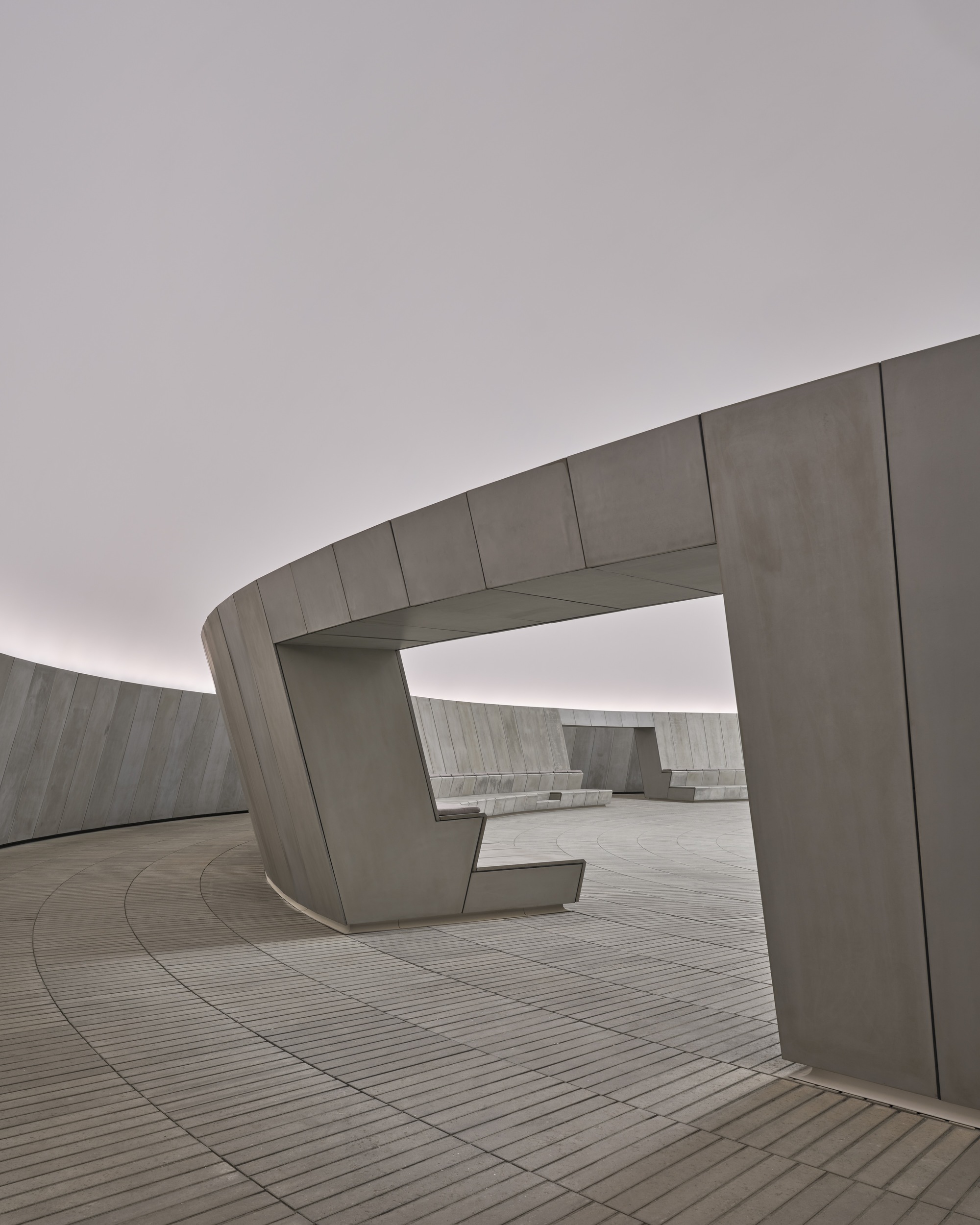 Precast concrete seating elements with angular forms arranged along the curved perimeter wall under cloudy skies
