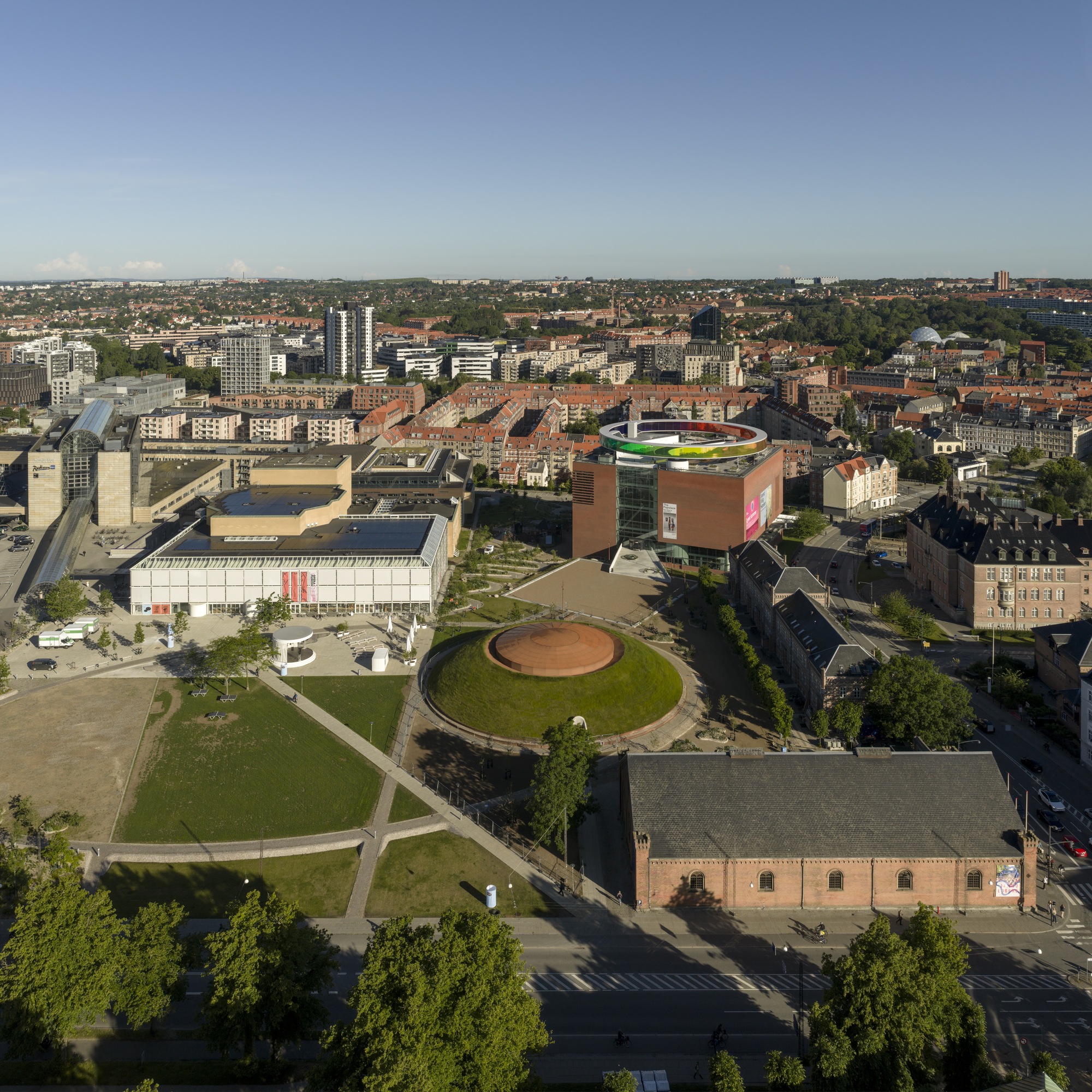 Aerial view showing the cylindrical museum building and circular rooftop plaza within the mixed urban neighborhood