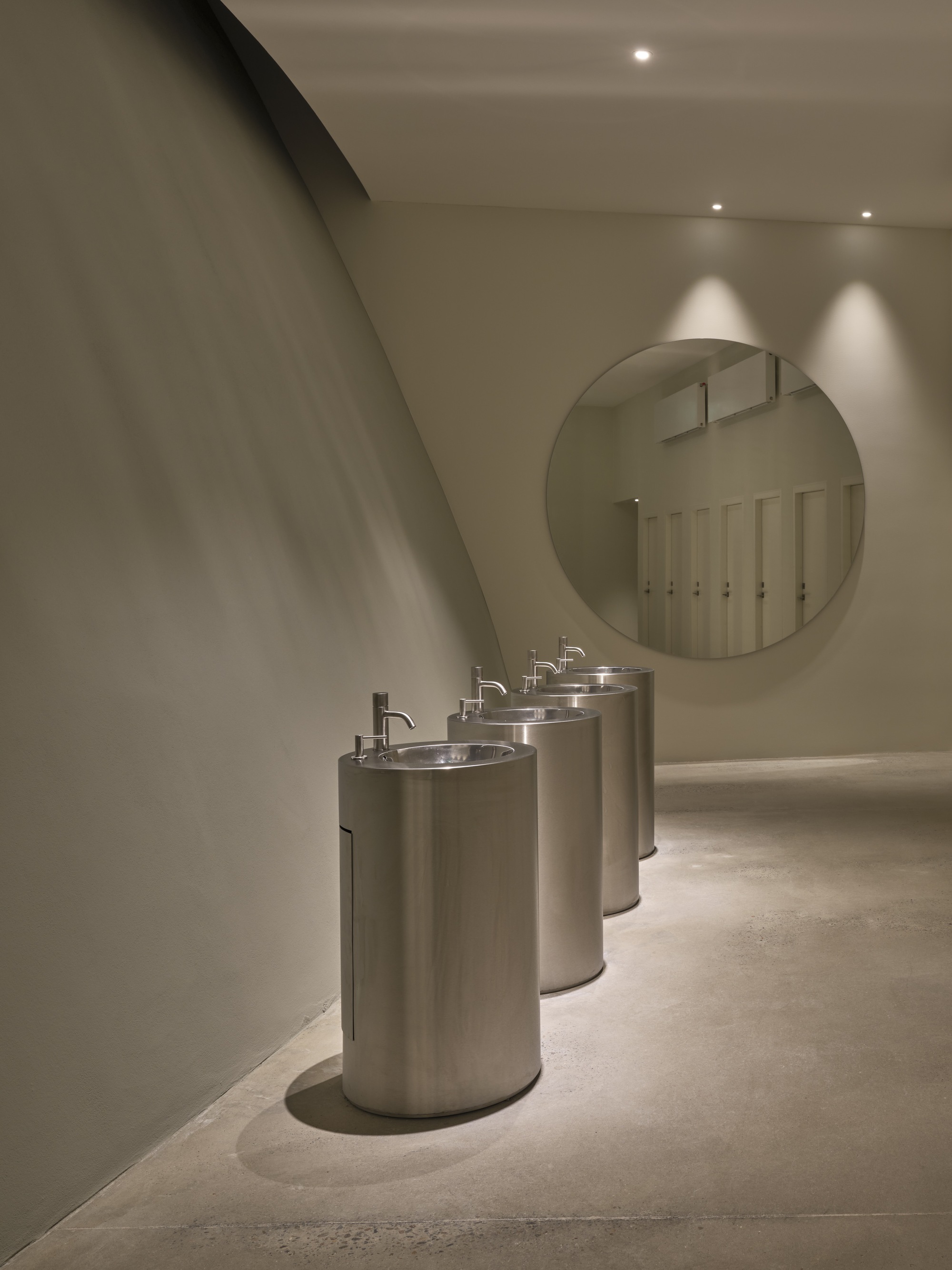 Curved corridor with cylindrical stainless steel drinking fountains beneath spotlights and a round mirror