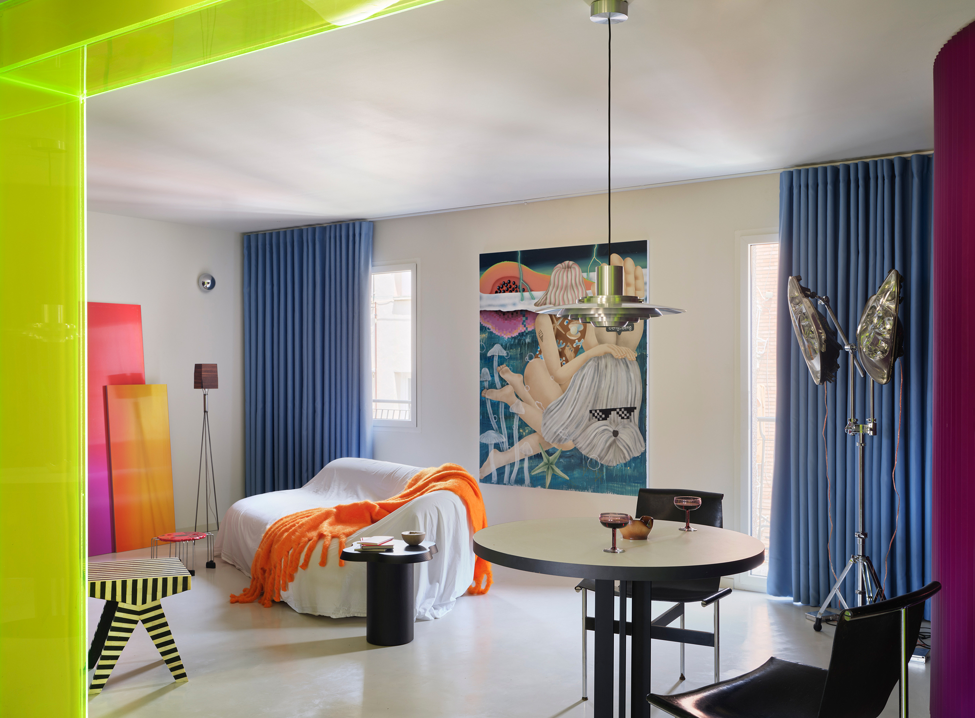 Open plan bedroom showing blue pleated curtains, artwork on walls, and lime green ceiling strip