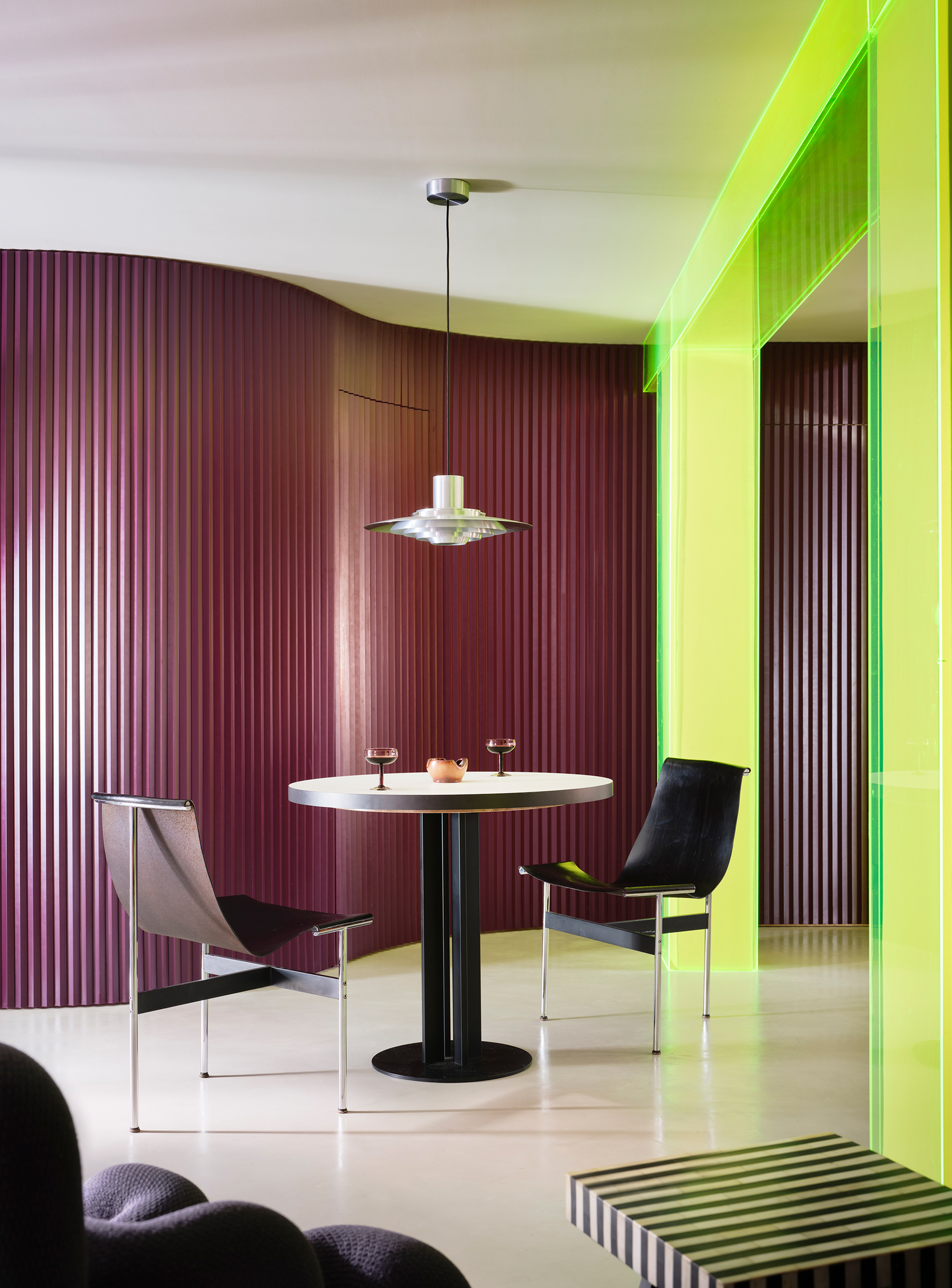 Dining area with curved purple corrugated wall and chartreuse portal framing a pedestal table under pendant light
