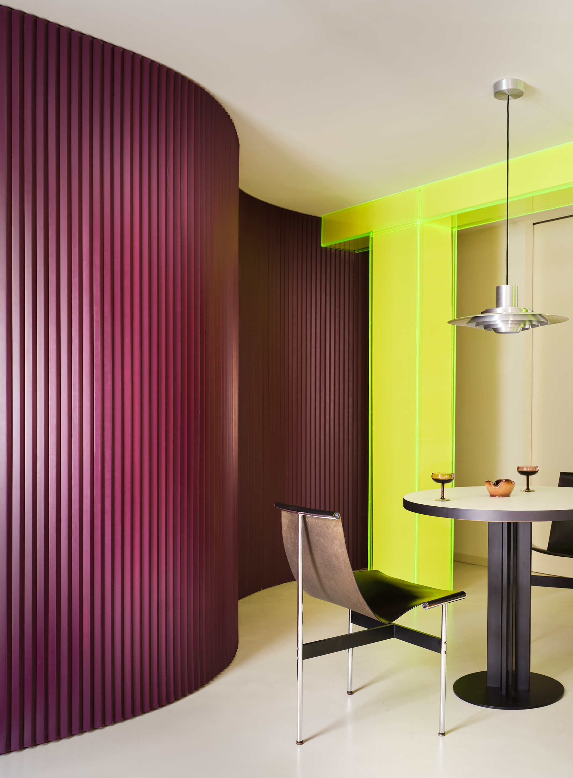 View through chartreuse frame showing curved purple corrugated partition and white dining table with pendant fixture