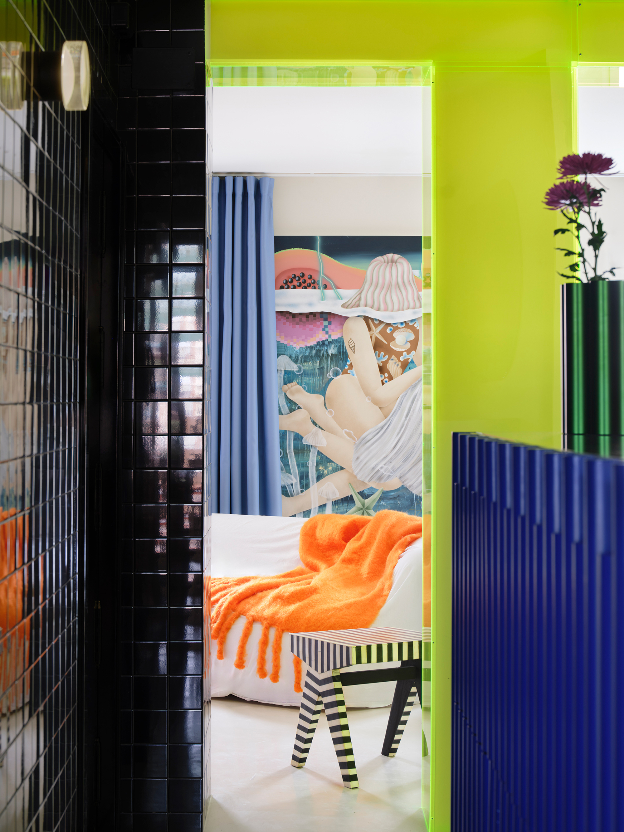 View through black tile and chartreuse doorway into bedroom with figurative artwork and striped stool