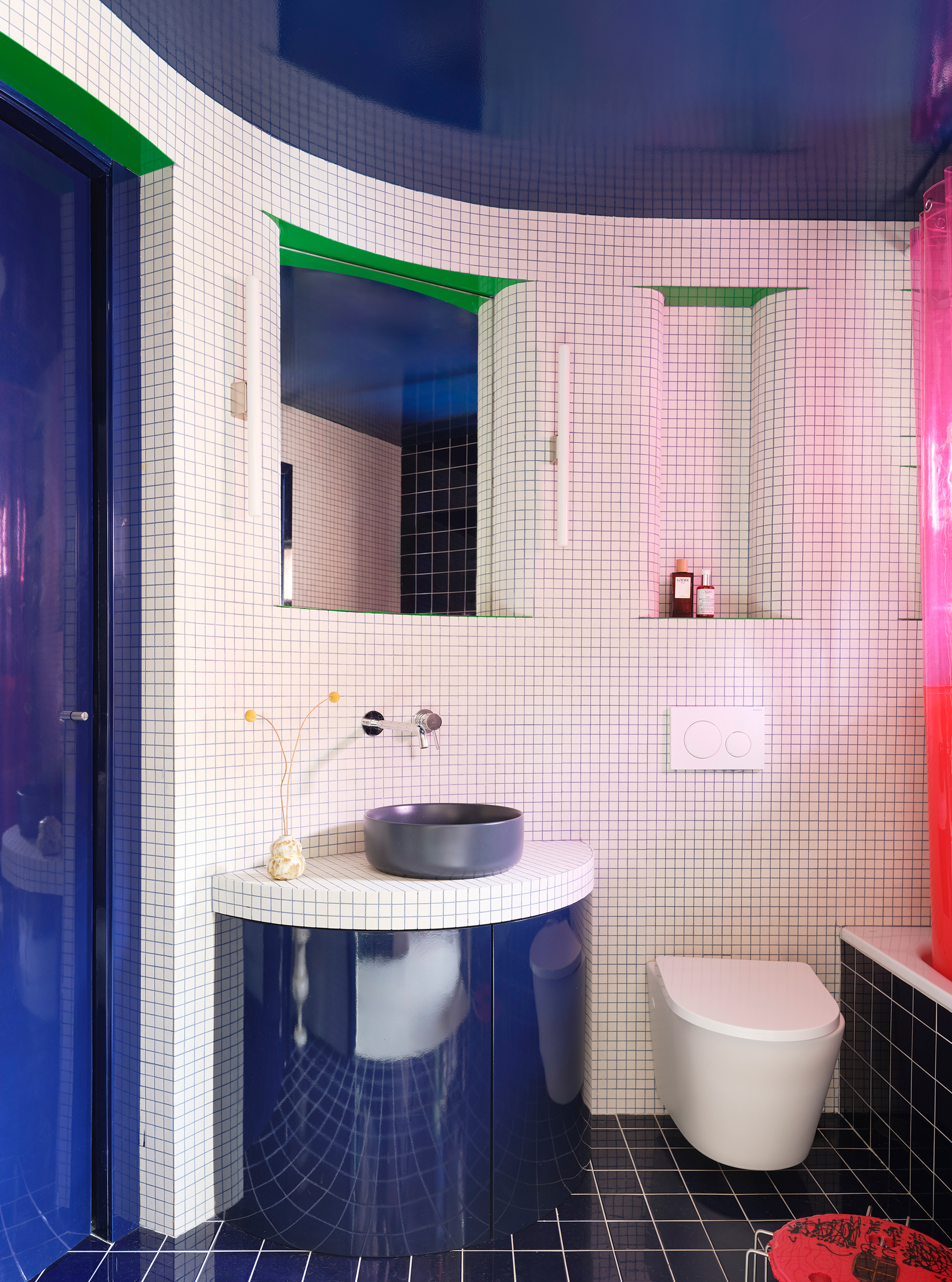 Bathroom with white mosaic tile walls, curved mirrors with green frames, and blue reflective surfaces