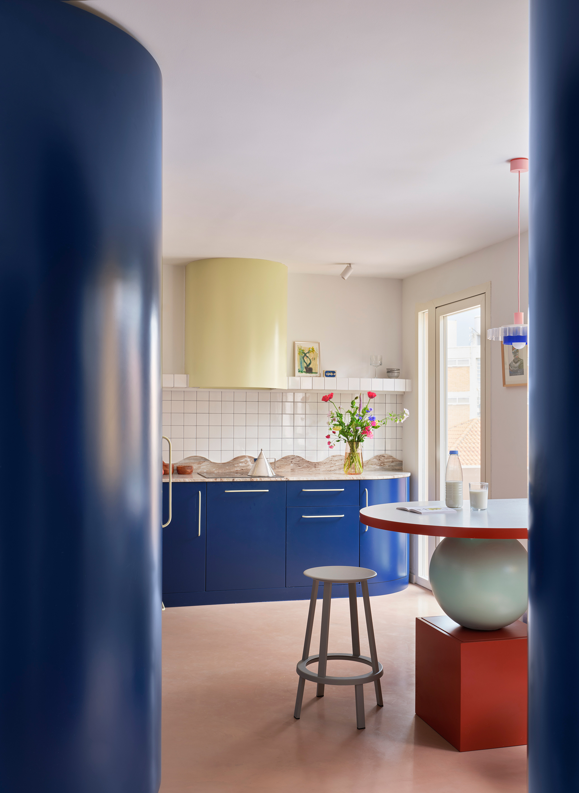 Kitchen view through blue columns showing white tile backsplash, blue cabinetry, and vase of flowers