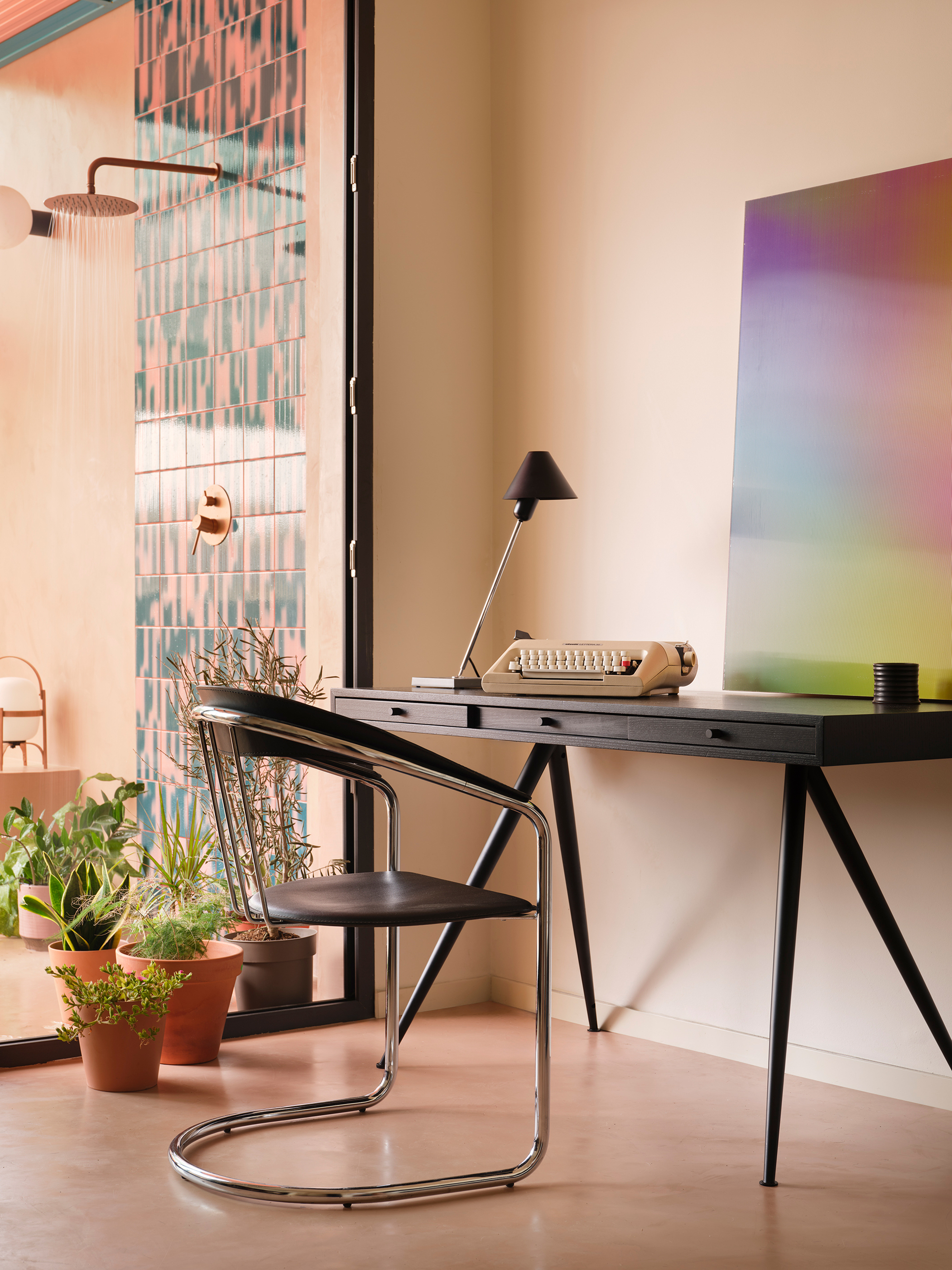 Black desk and chrome cantilever chair beside glazed wall with pink and turquoise chequered tile pattern