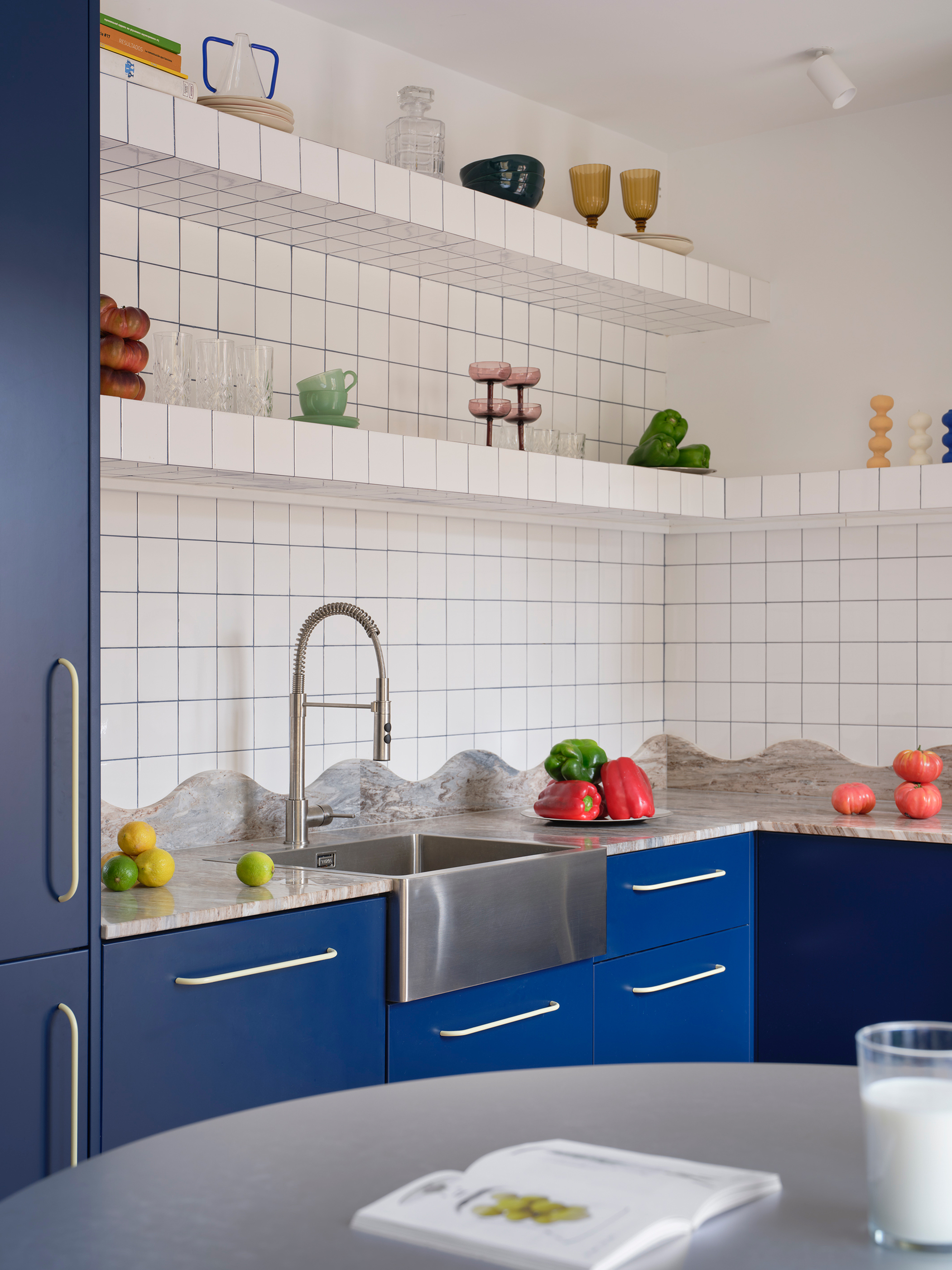 Corner kitchen with blue cabinets, white square tile backsplash, and open shelves displaying glassware and plants
