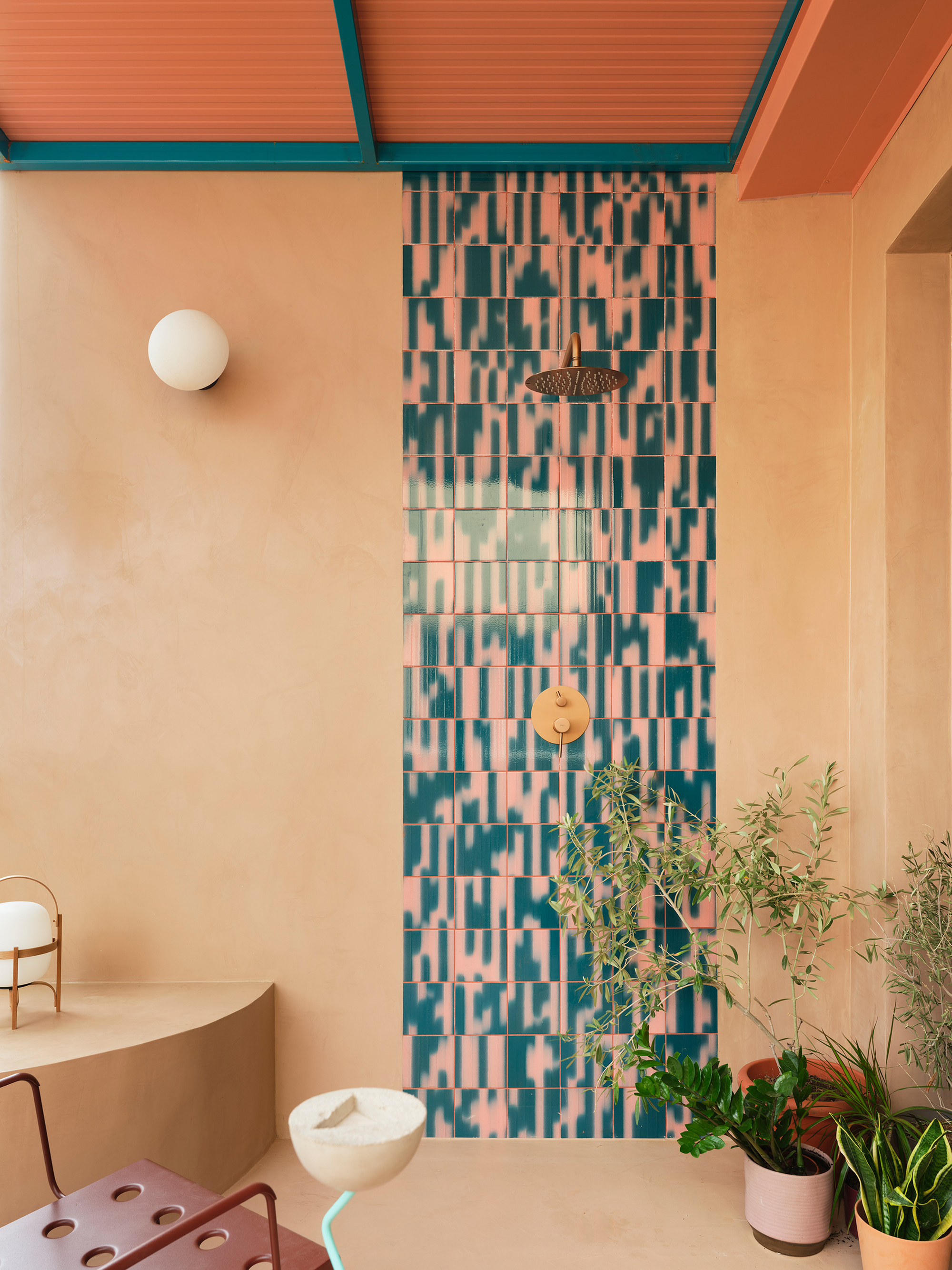 Bathroom shower wall with pink and teal mosaic tile beneath peach ceiling and potted plants at floor