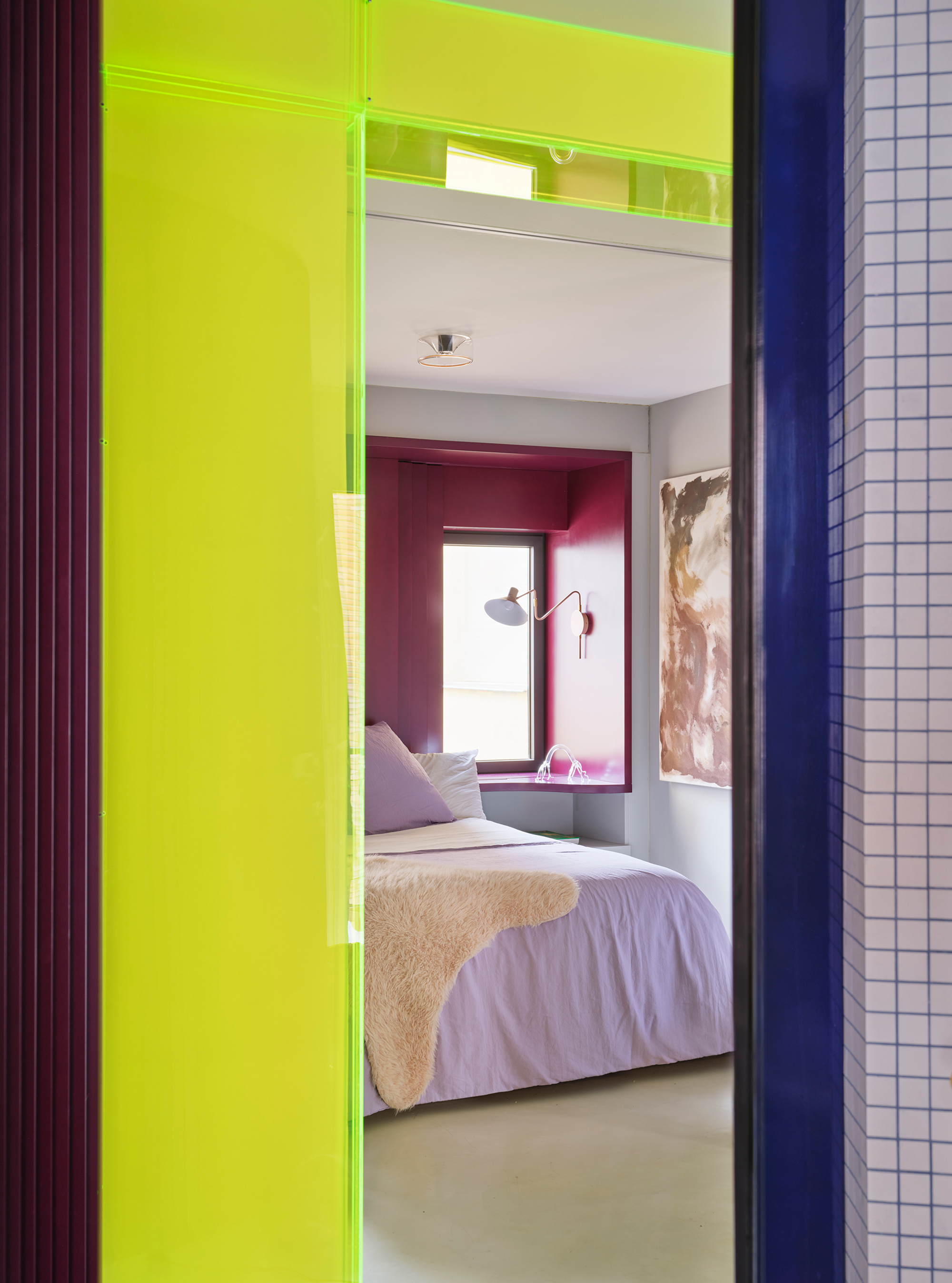 View through lime green doorway into bedroom with deep burgundy window alcove and white grid tile partition
