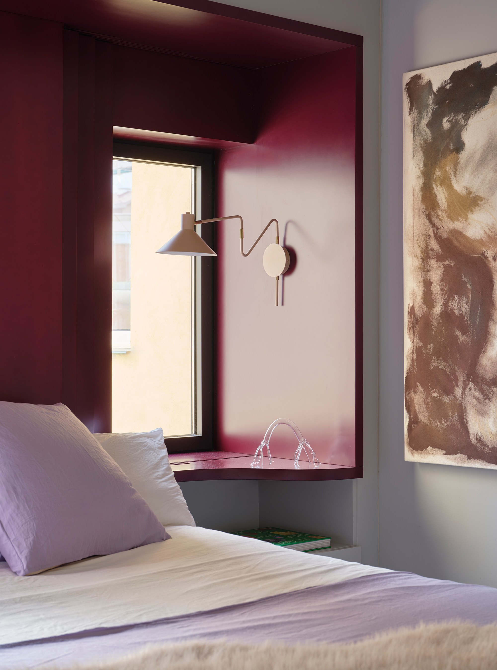 Bedroom window alcove painted burgundy with wall-mounted lamp and sunlight filtering through the frame