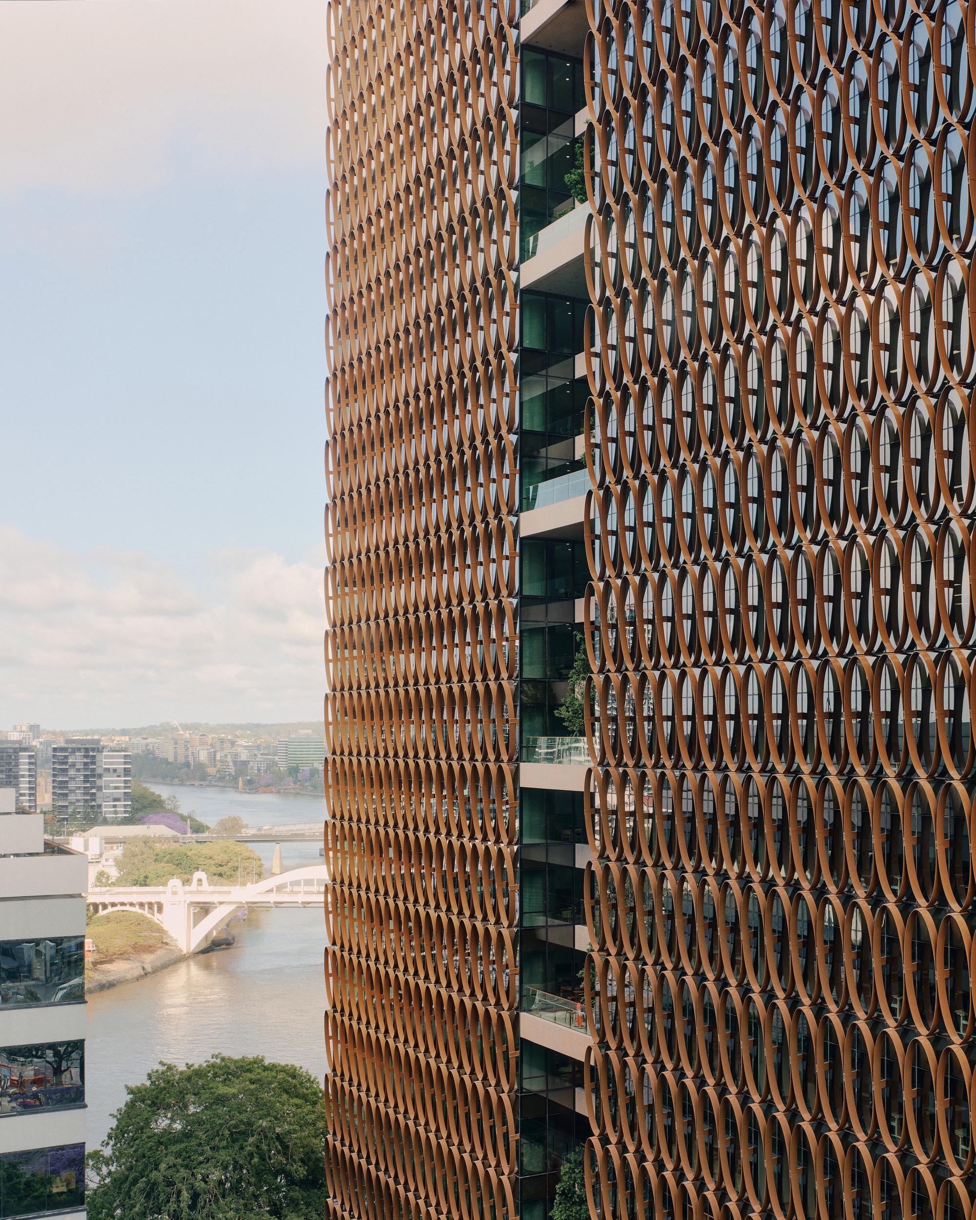 Curved tower facade with repeating bronze oval screens and recessed balconies overlooking the river below
