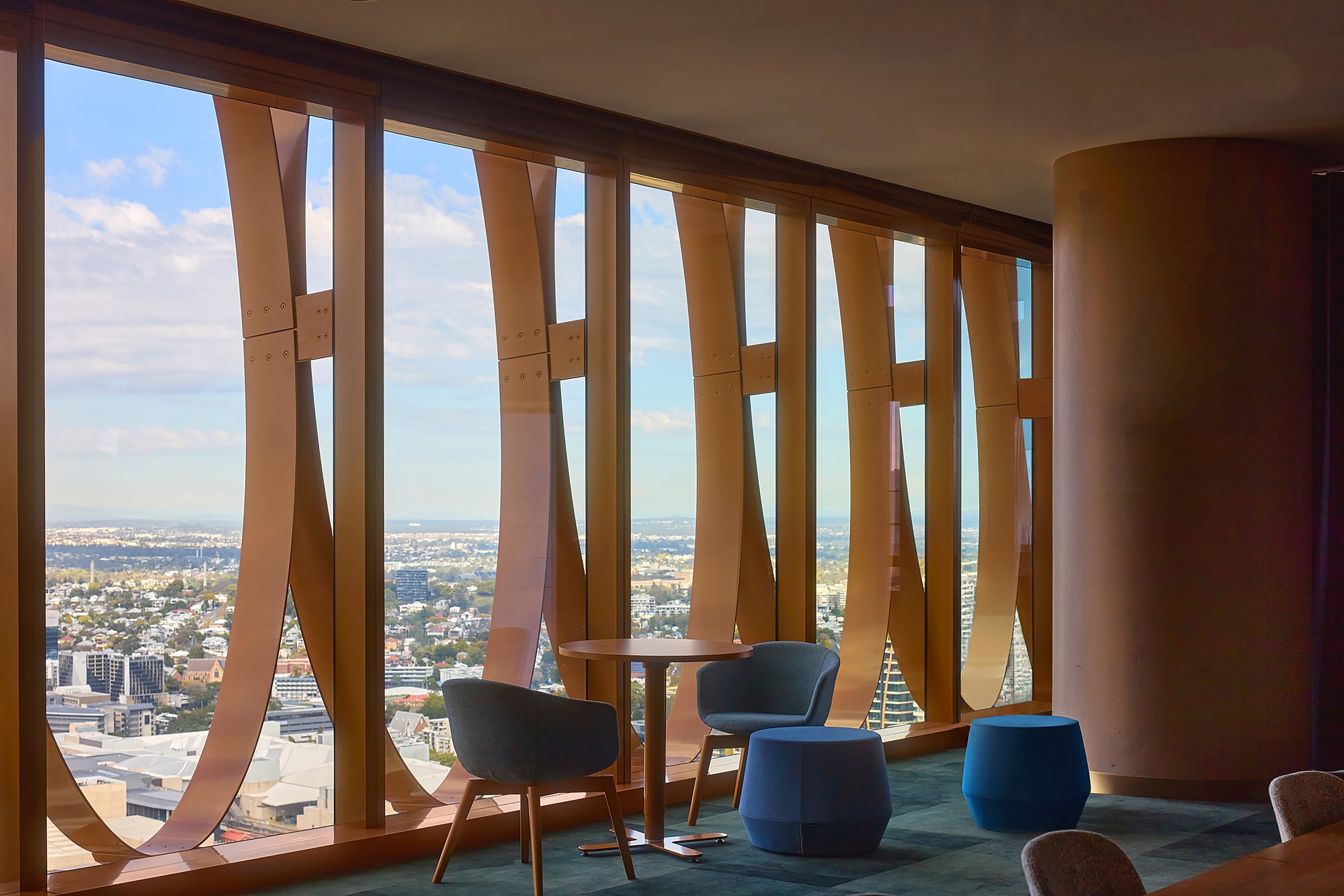 Interior lounge with curved timber screen and blue upholstered chairs overlooking the cityscape through floor-to-ceiling windows