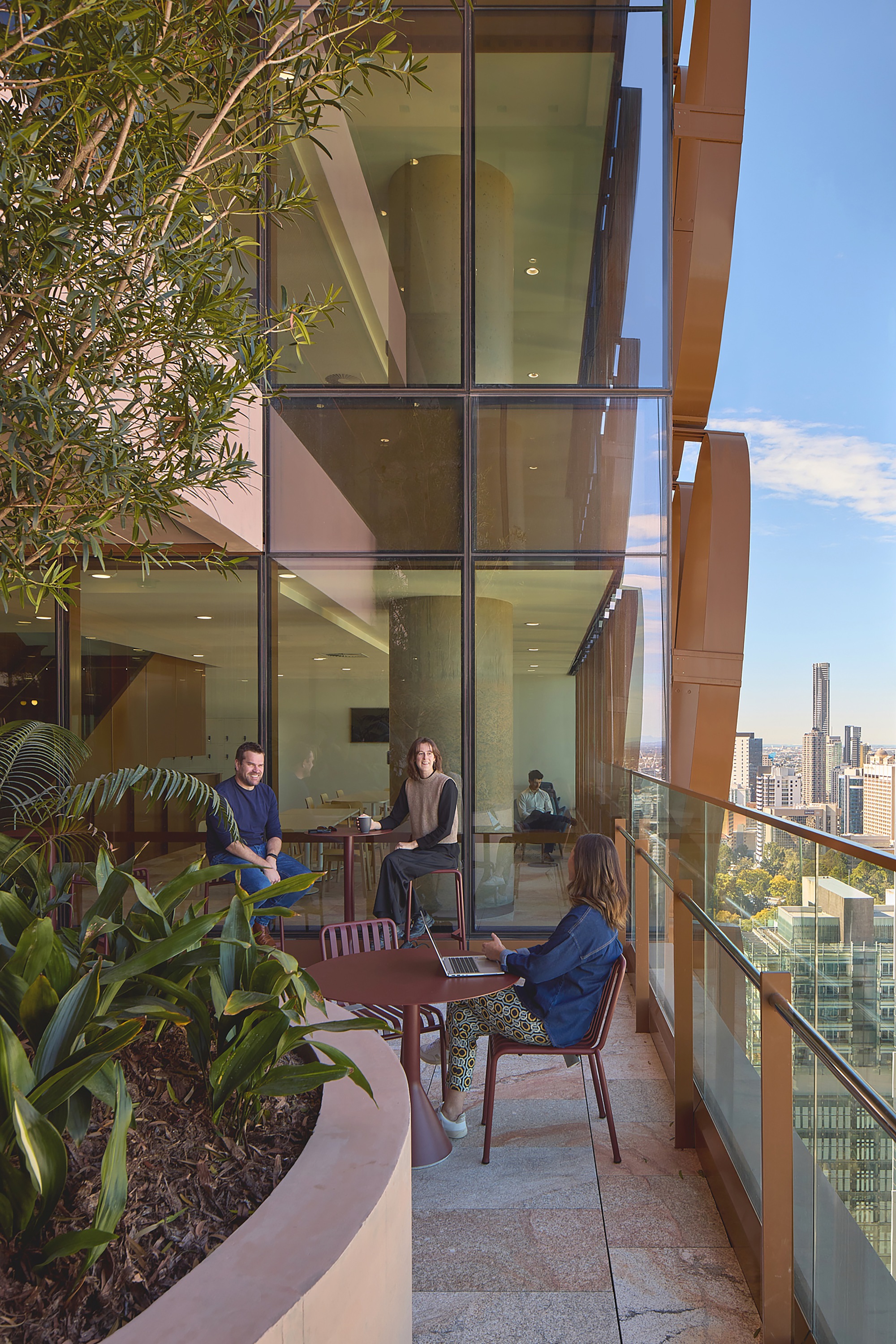 Glass-enclosed terrace with planted bed and people seated at tables overlooking the city skyline on a clear day