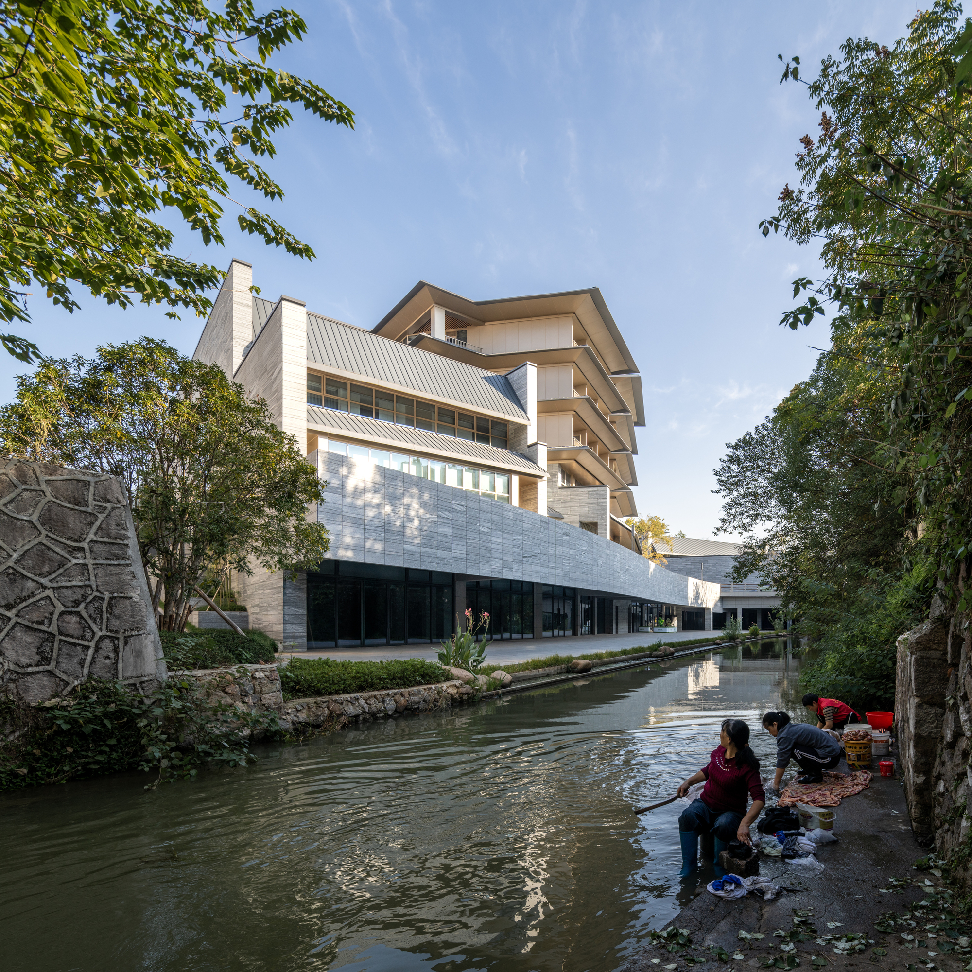 Tiered volume with metal roof and stone base rising above the canal with people washing clothes