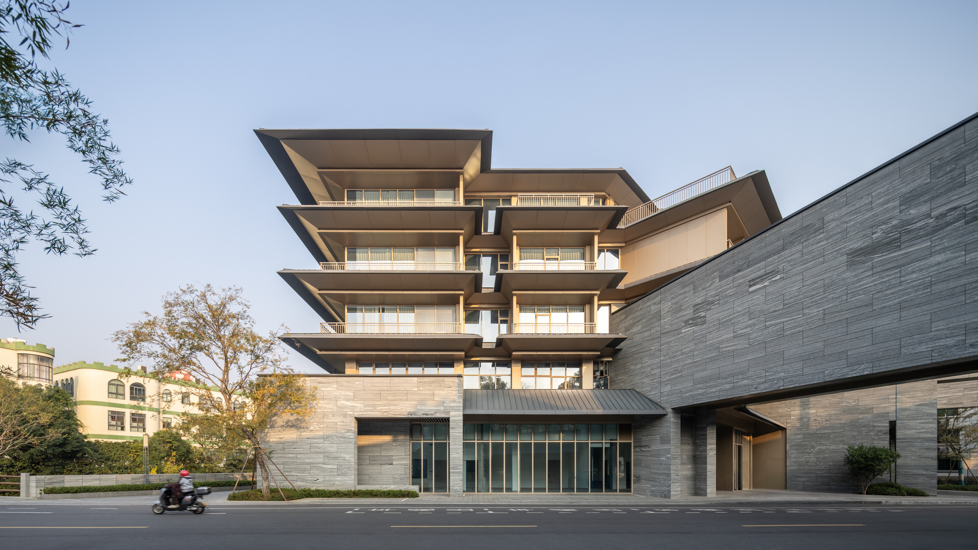 Street view of the stacked horizontal slabs with deep overhangs above the grey stone base