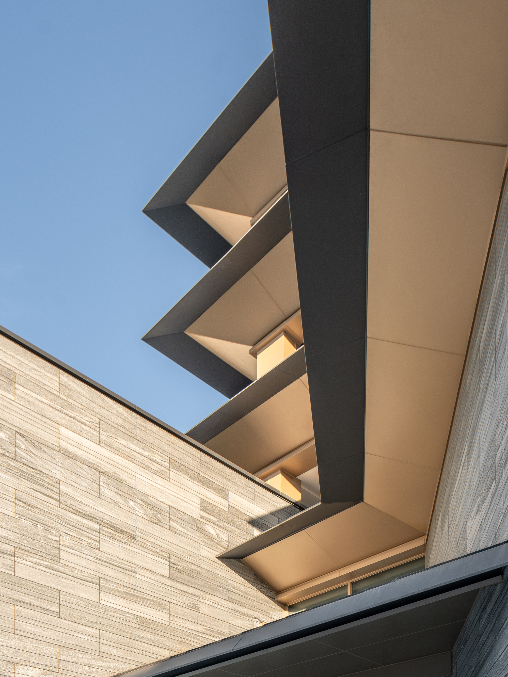 Upward view of the stacked cantilevered roof planes with recessed lighting against clear sky