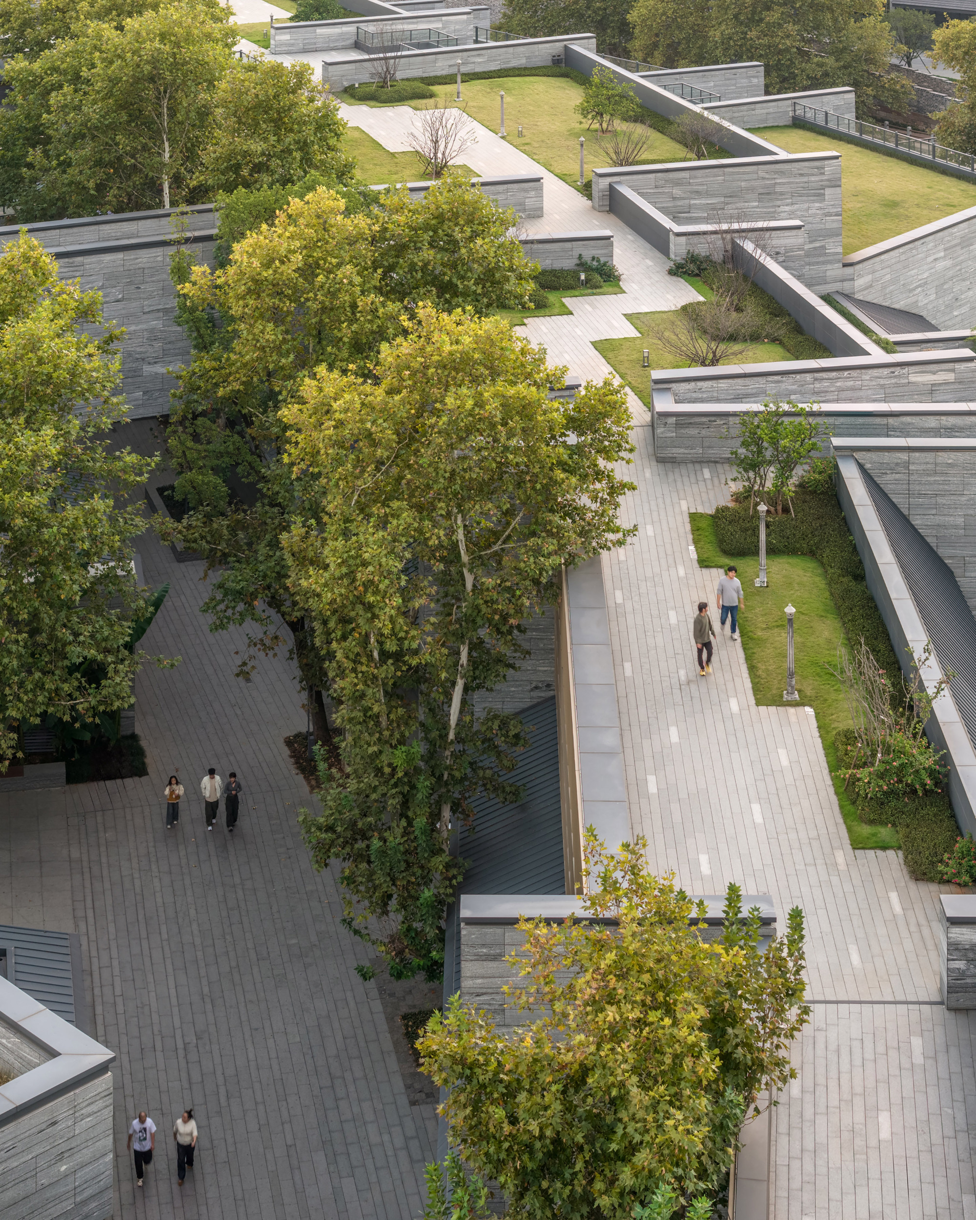 Aerial view of terraced stone pavilions with green roofs and mature trees along paved walkways