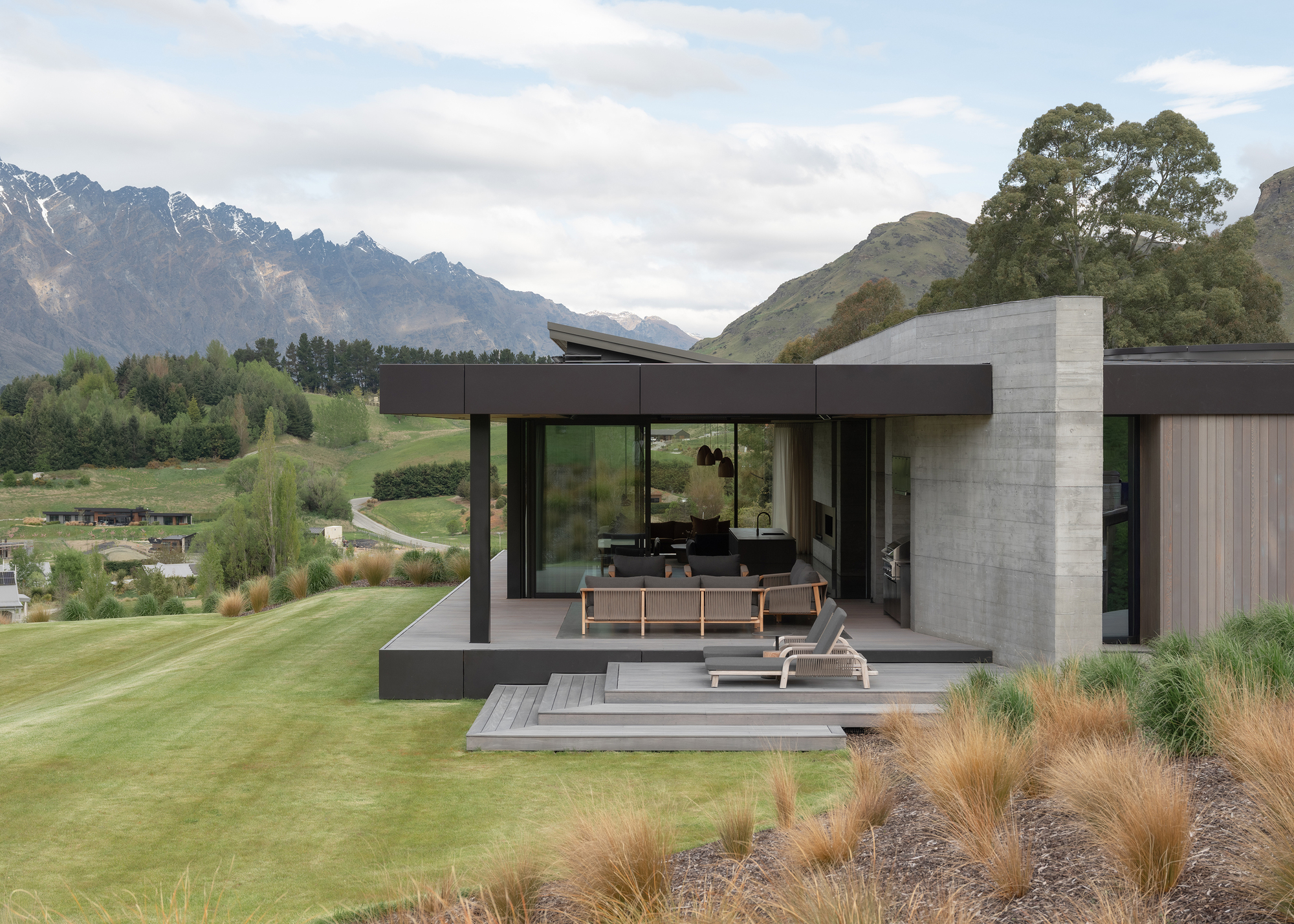 Covered terrace with timber deck and loungers facing a lawn and distant mountain range