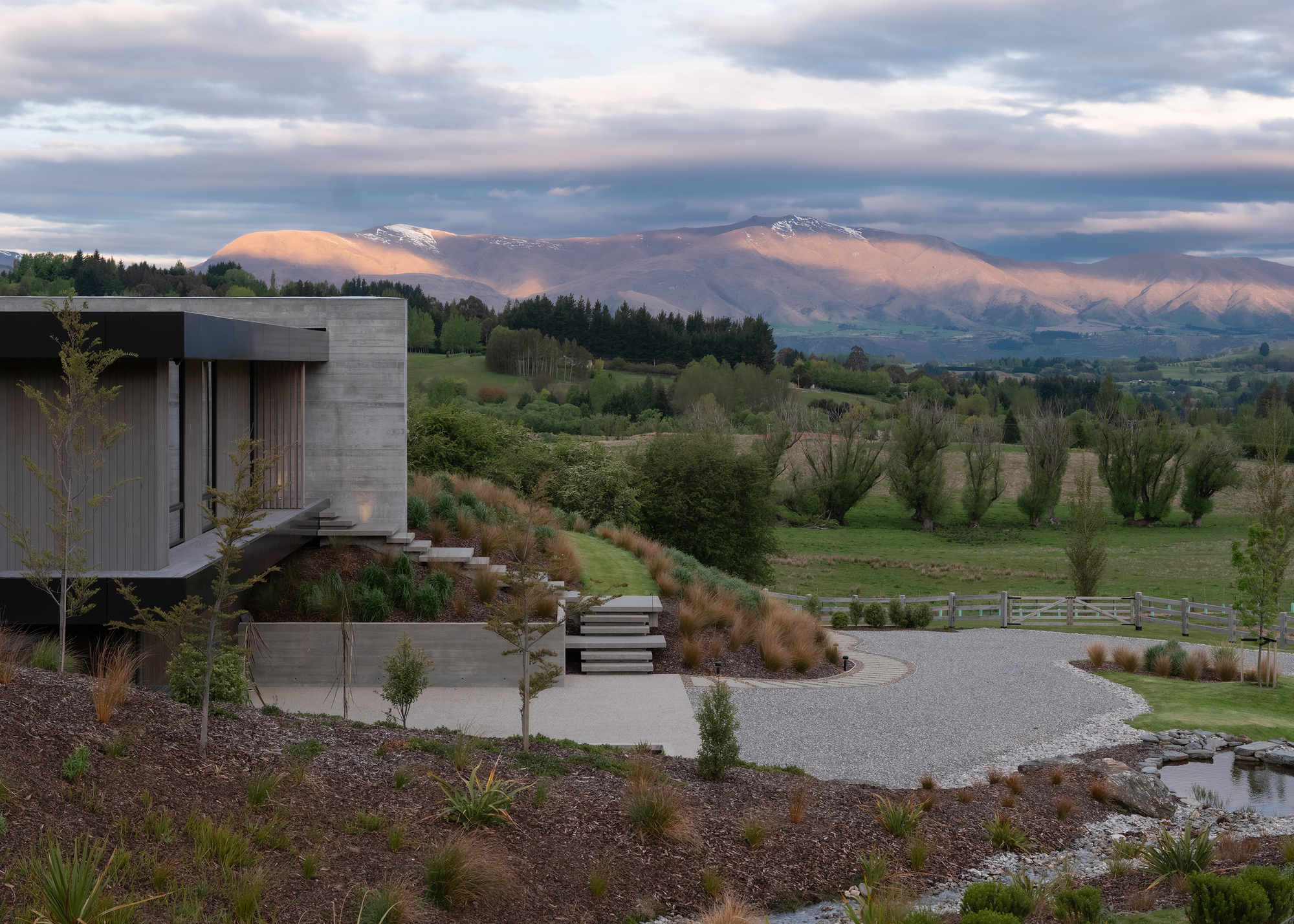 Gravel motor court and landscaped berms viewed at dusk with snow-capped peaks in the distance