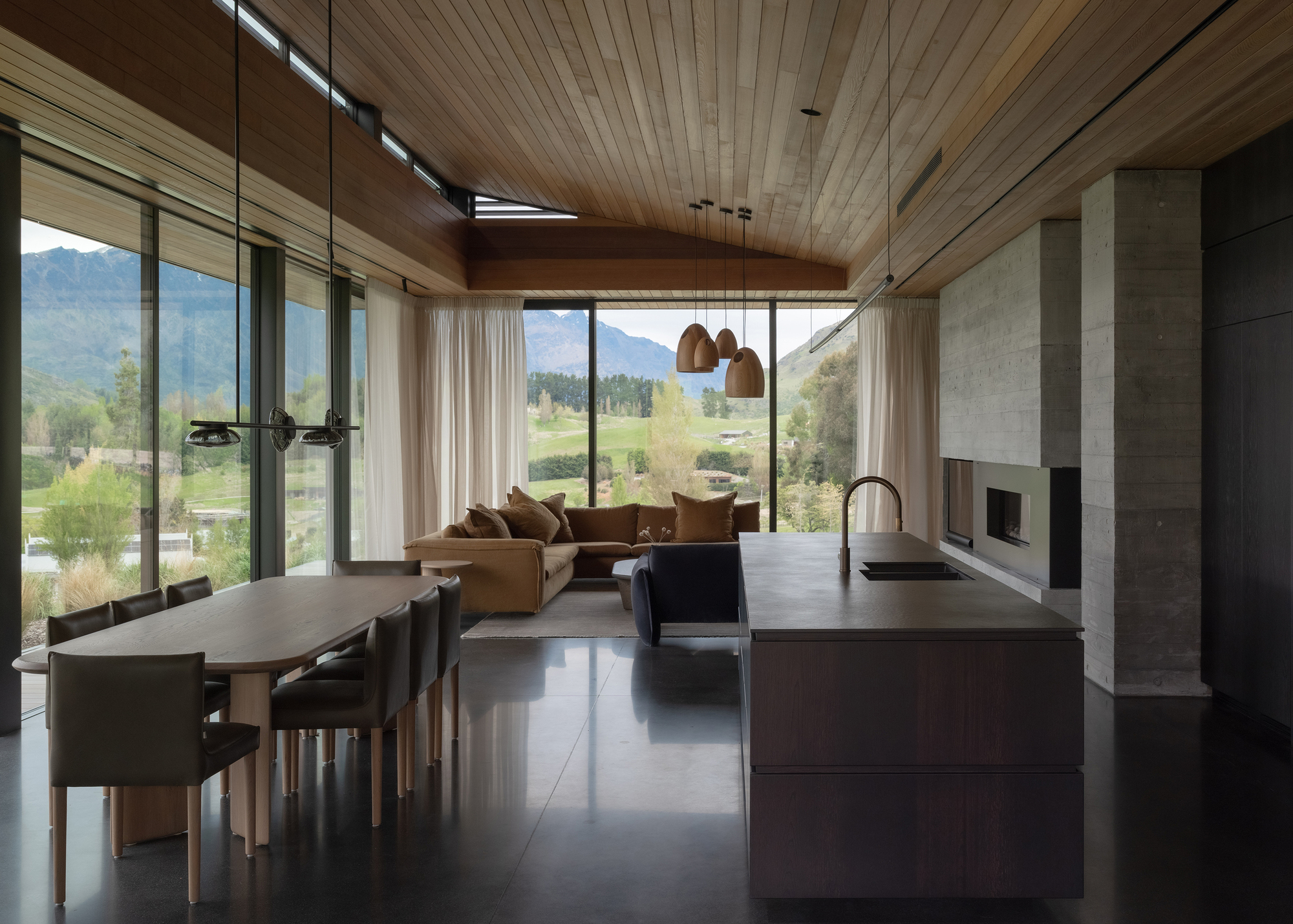Open-plan living space with timber ceiling, floor-to-ceiling glazing and mountain views through multiple openings