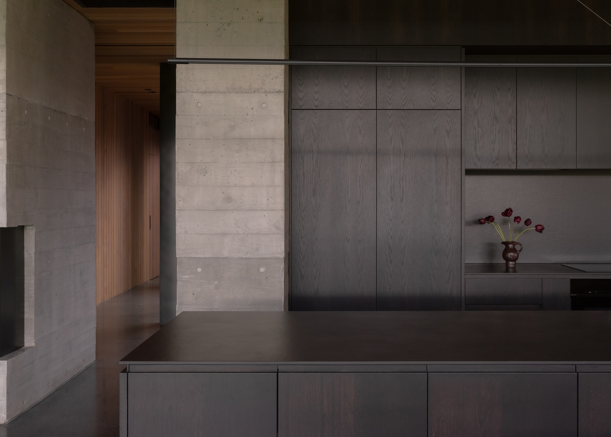 Kitchen counter detail showing dark timber cabinetry, concrete pillar and small vase with purple flowers