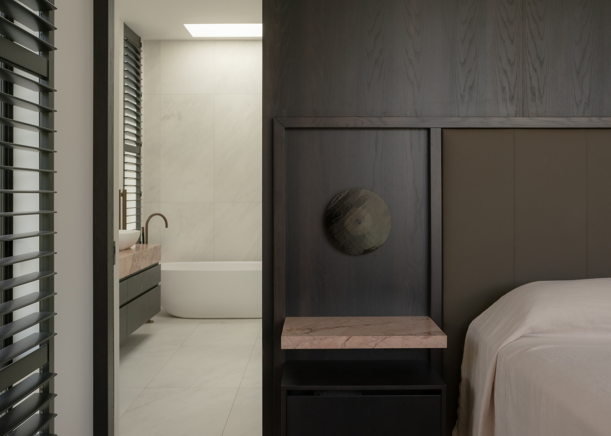 Bedroom with timber-framed sleeping niche and adjacent ensuite bathroom glimpsed through doorway with horizontal louvres