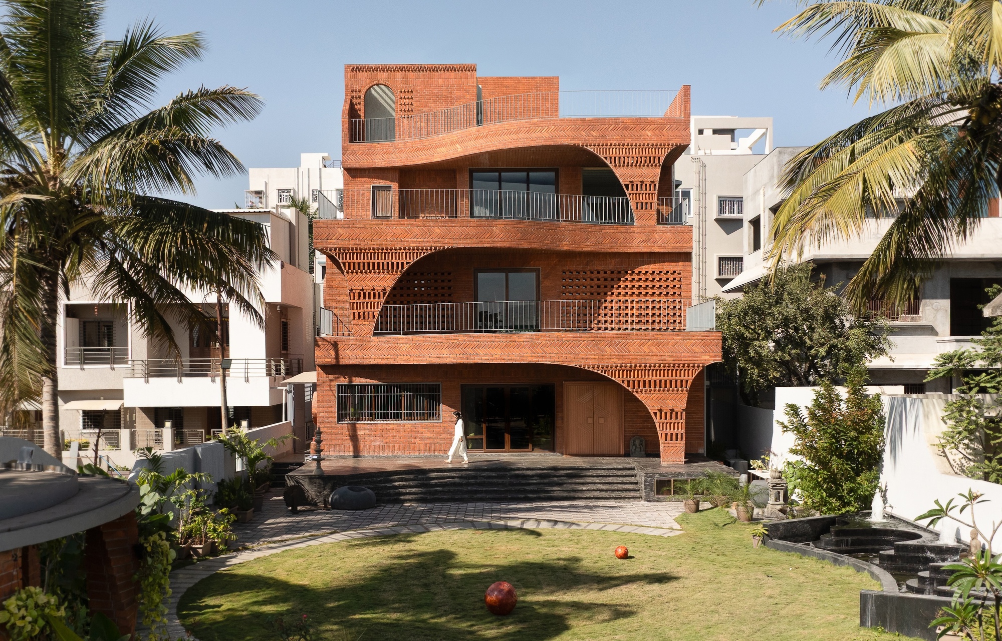 Street view of the terracotta brick facade with curved balconies framed by coconut palms and lawn