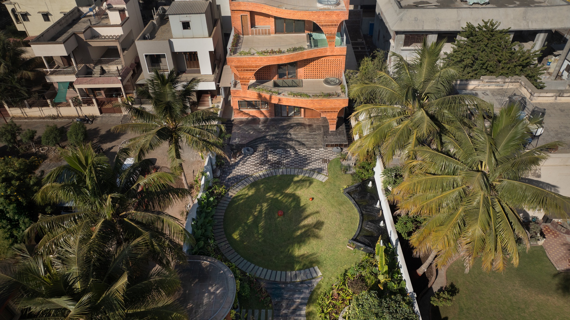 Aerial view of the curved terracotta residence with tiered garden and surrounding palm trees