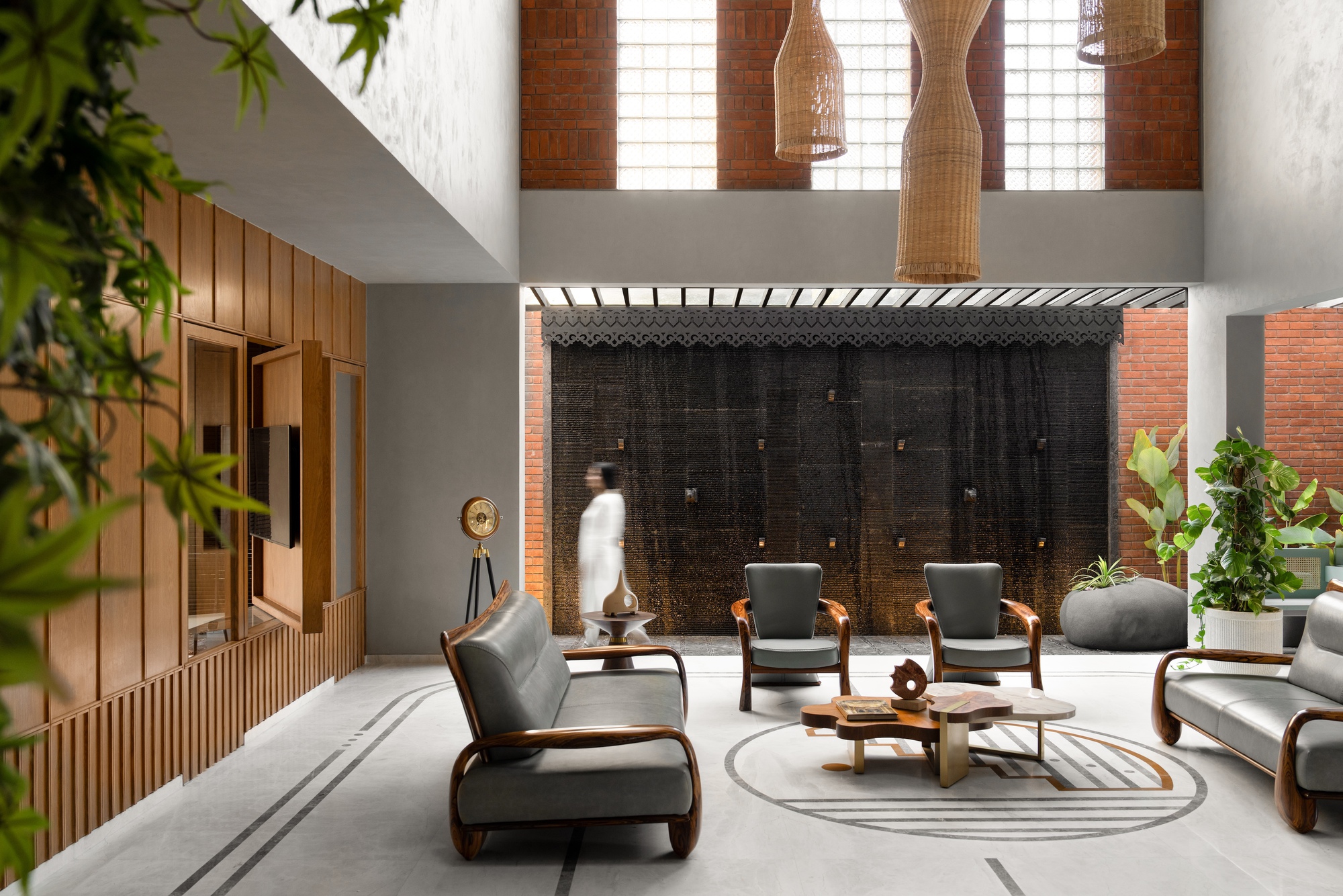 Interior courtyard with seating area beneath woven pendant lights and water feature wall with foliage