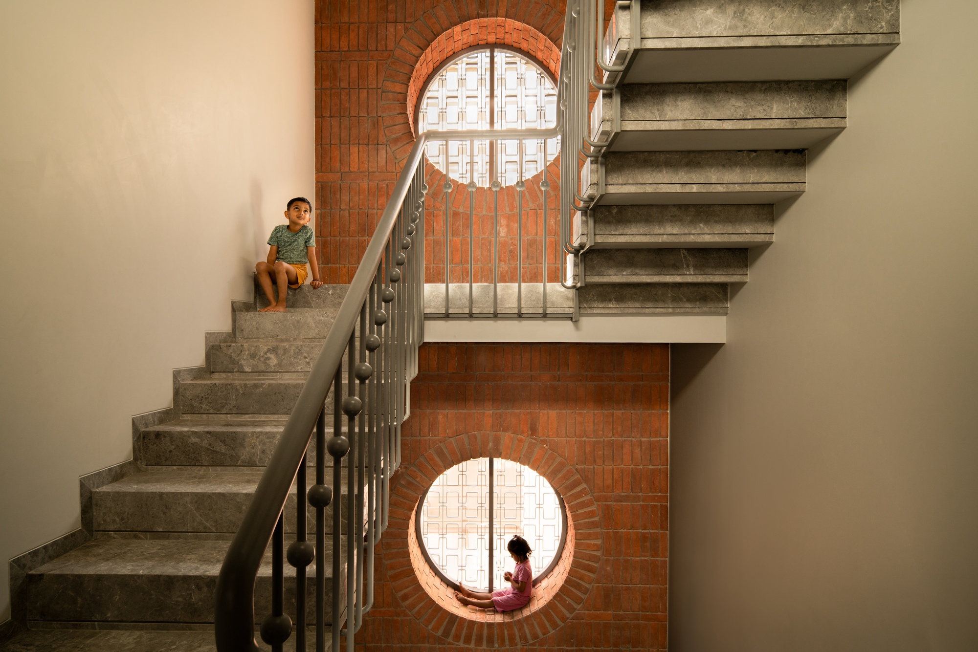 Concrete staircase with circular brick-framed windows where two children sit in natural light