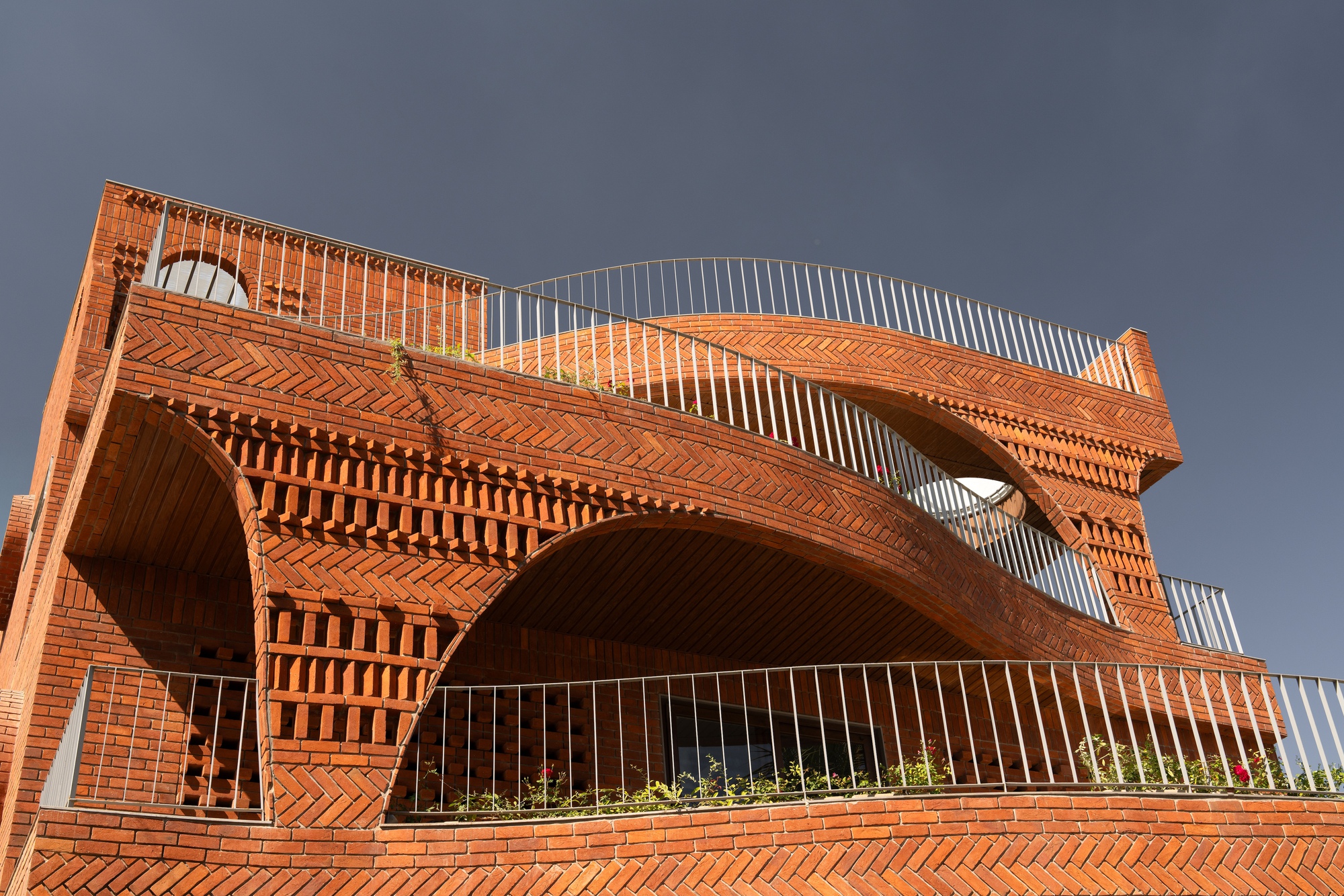 Cantilevered brick arches and diagonal brickwork patterns spanning the upper facade under dark sky