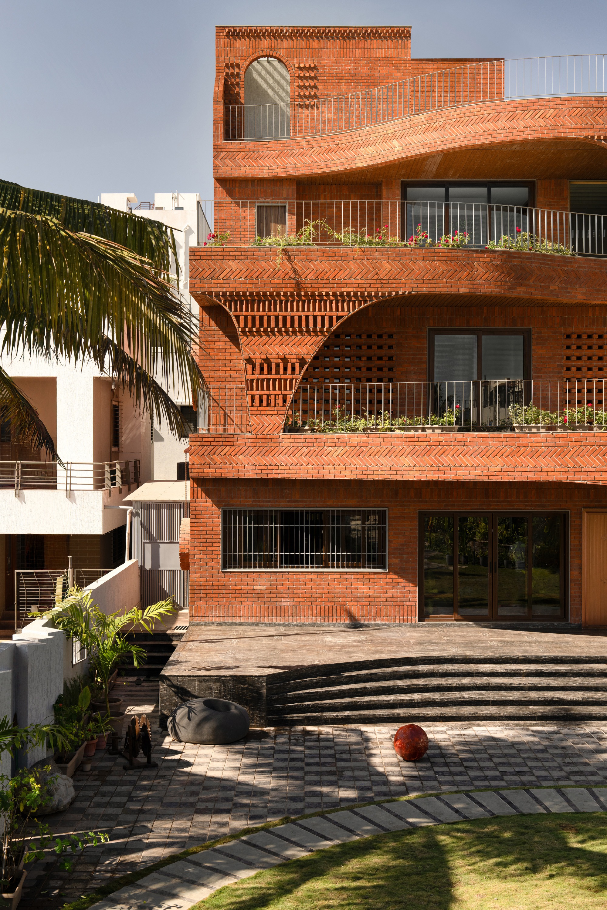 Multi-level brick facade with planted balconies and palm fronds framing the stepped courtyard below