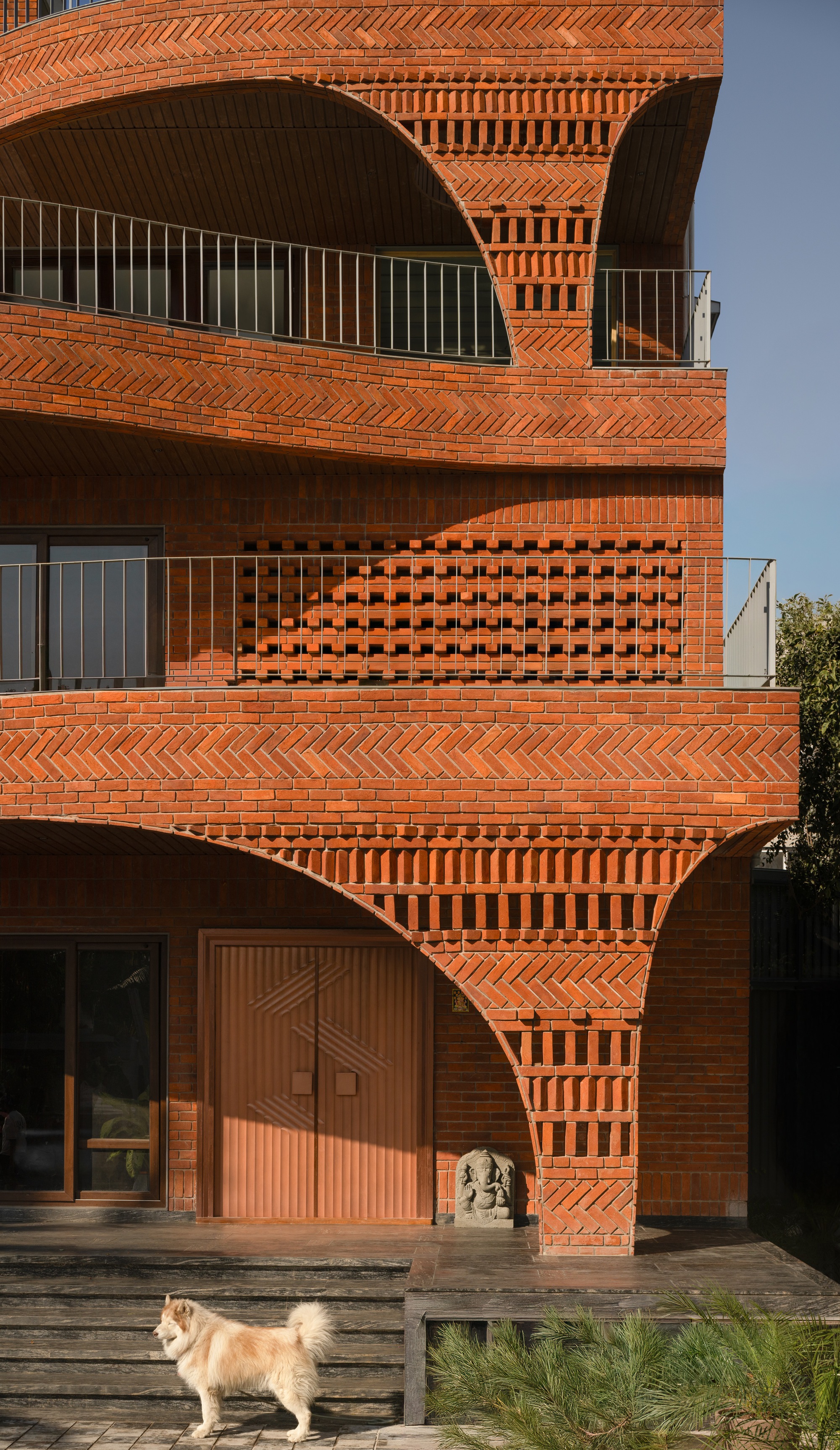 Layered terracotta brick patterns with perforated screens and timber door at ground level with dog