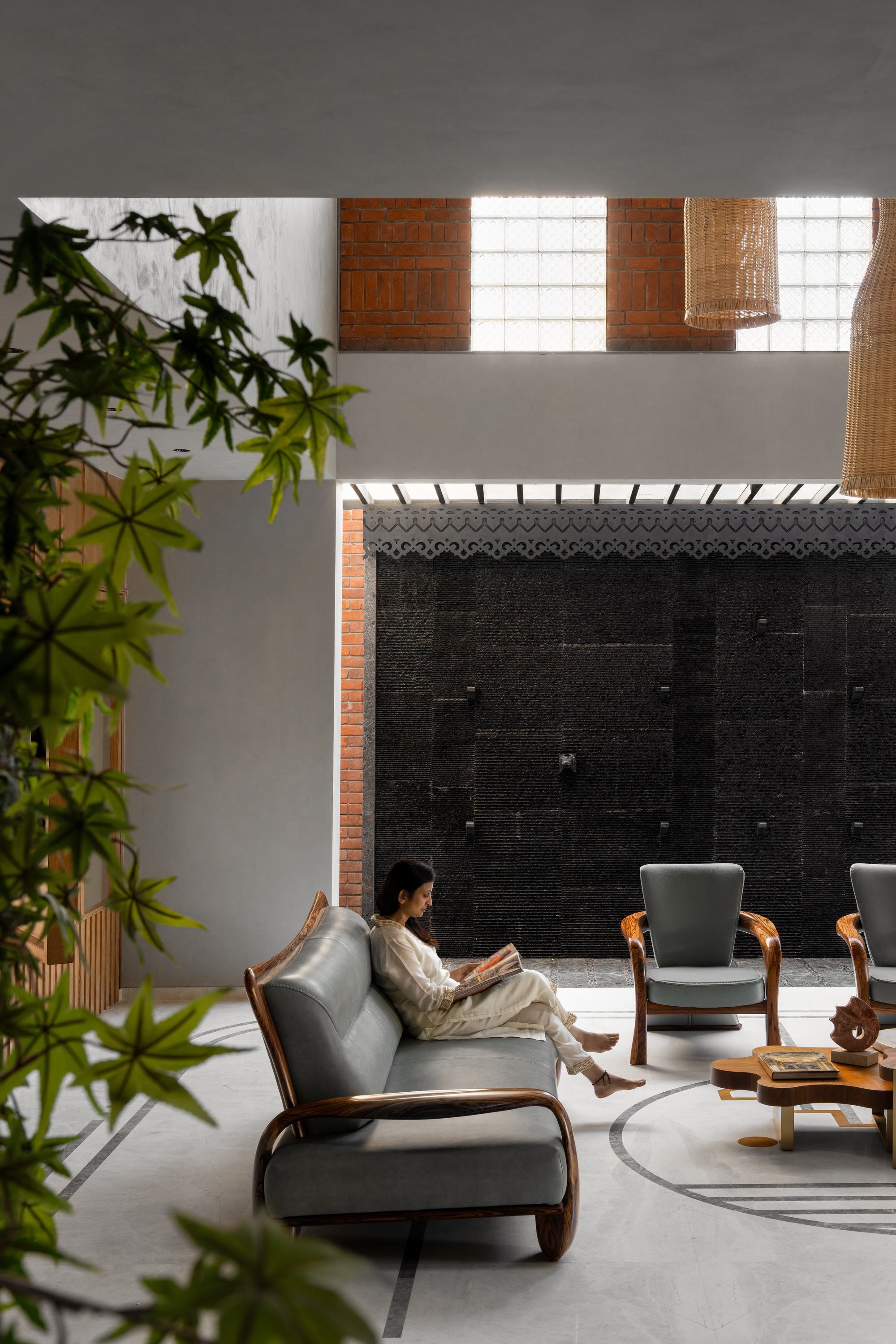 Interior courtyard with woman reading on lounge chair beneath clerestory windows and black tile wall