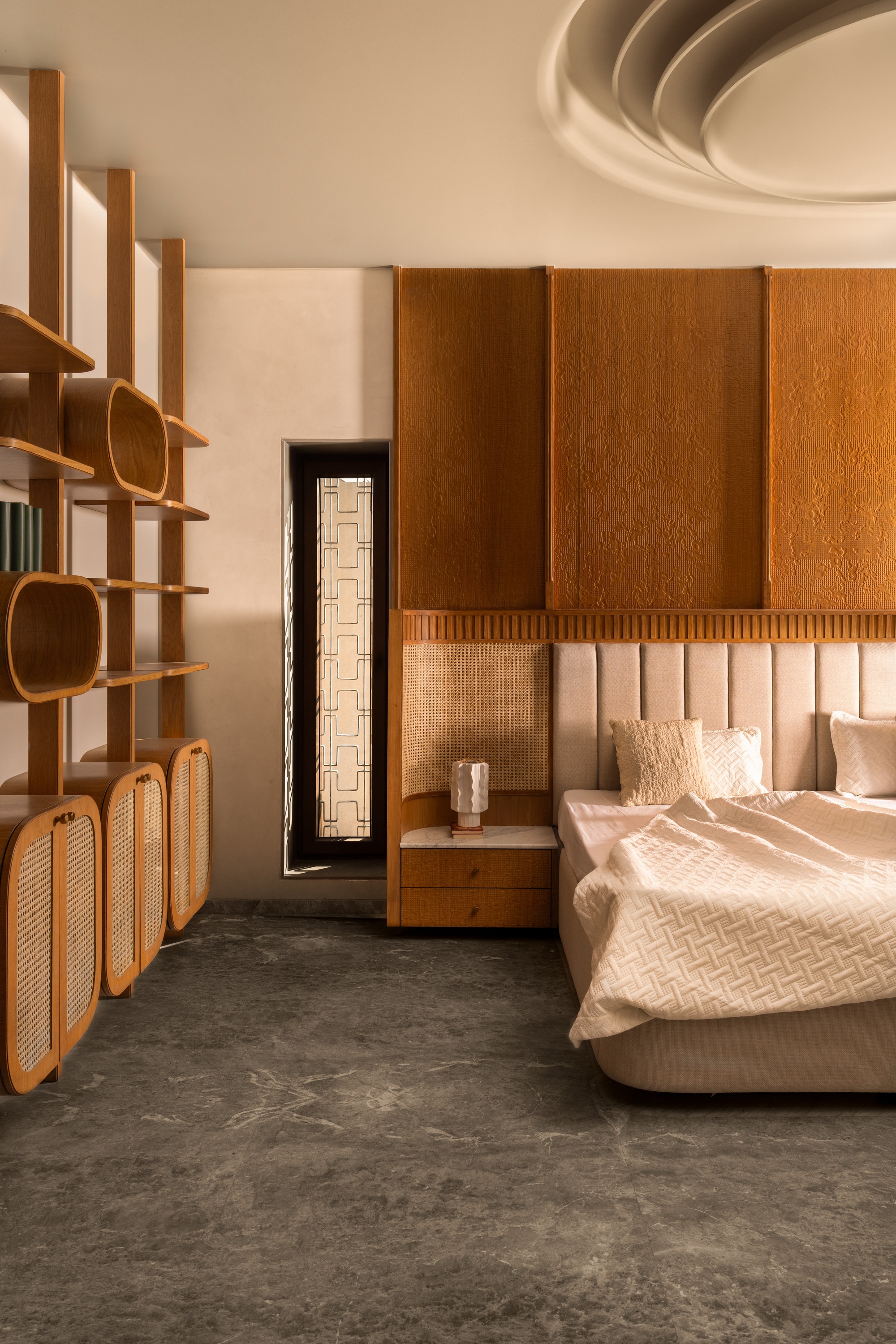 Bedroom with curved timber shelving unit, cane storage panels, and upholstered headboard in afternoon light