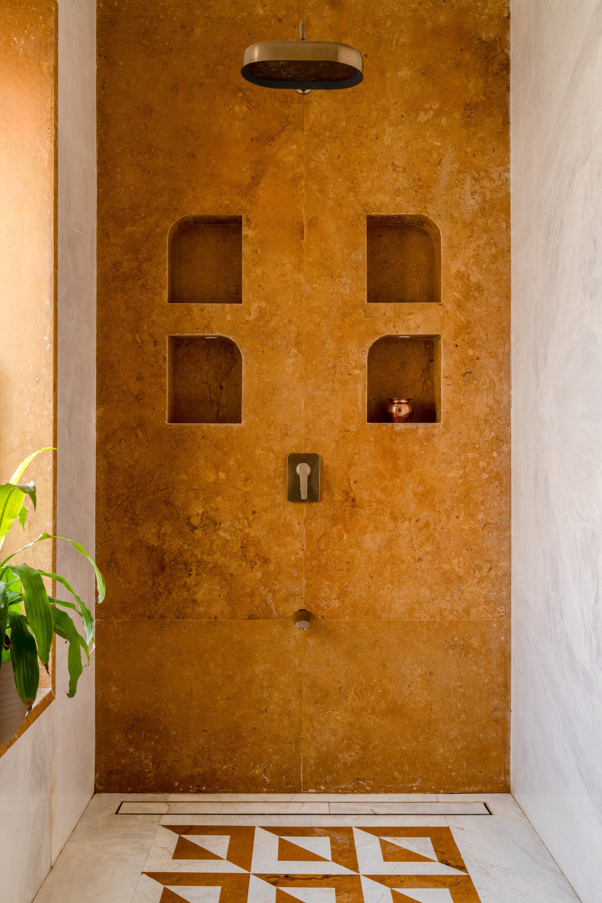 Textured ochre shower wall with four recessed niches above rainfall showerhead and geometric tile floor