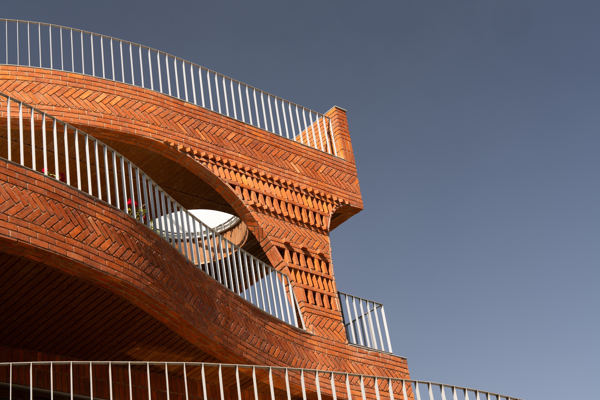 Exterior detail of layered brick facade with circular opening and vertical metal screen against a grey sky