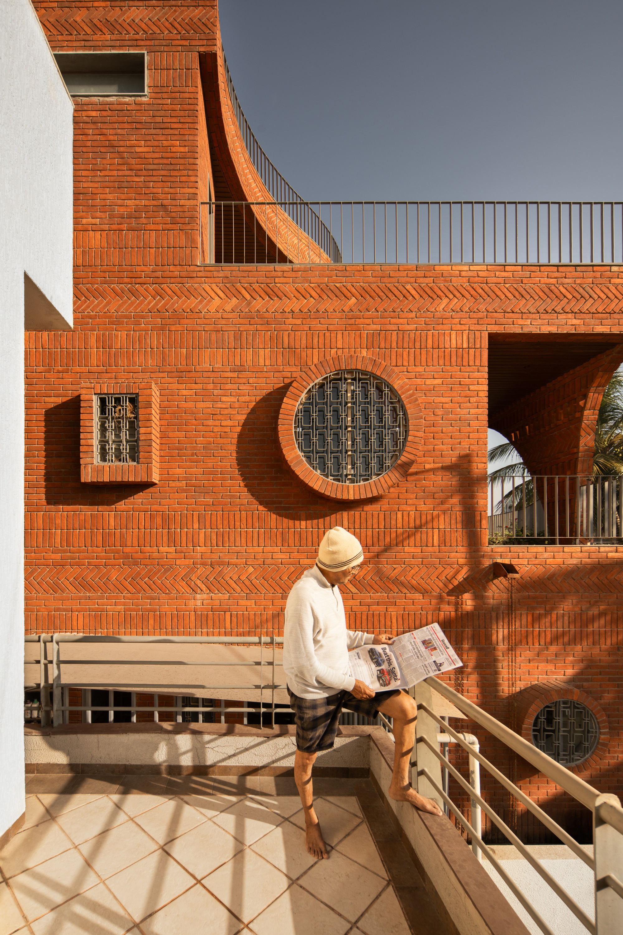 Herringbone brick facade with circular window and resident reading on a tiled terrace at midday