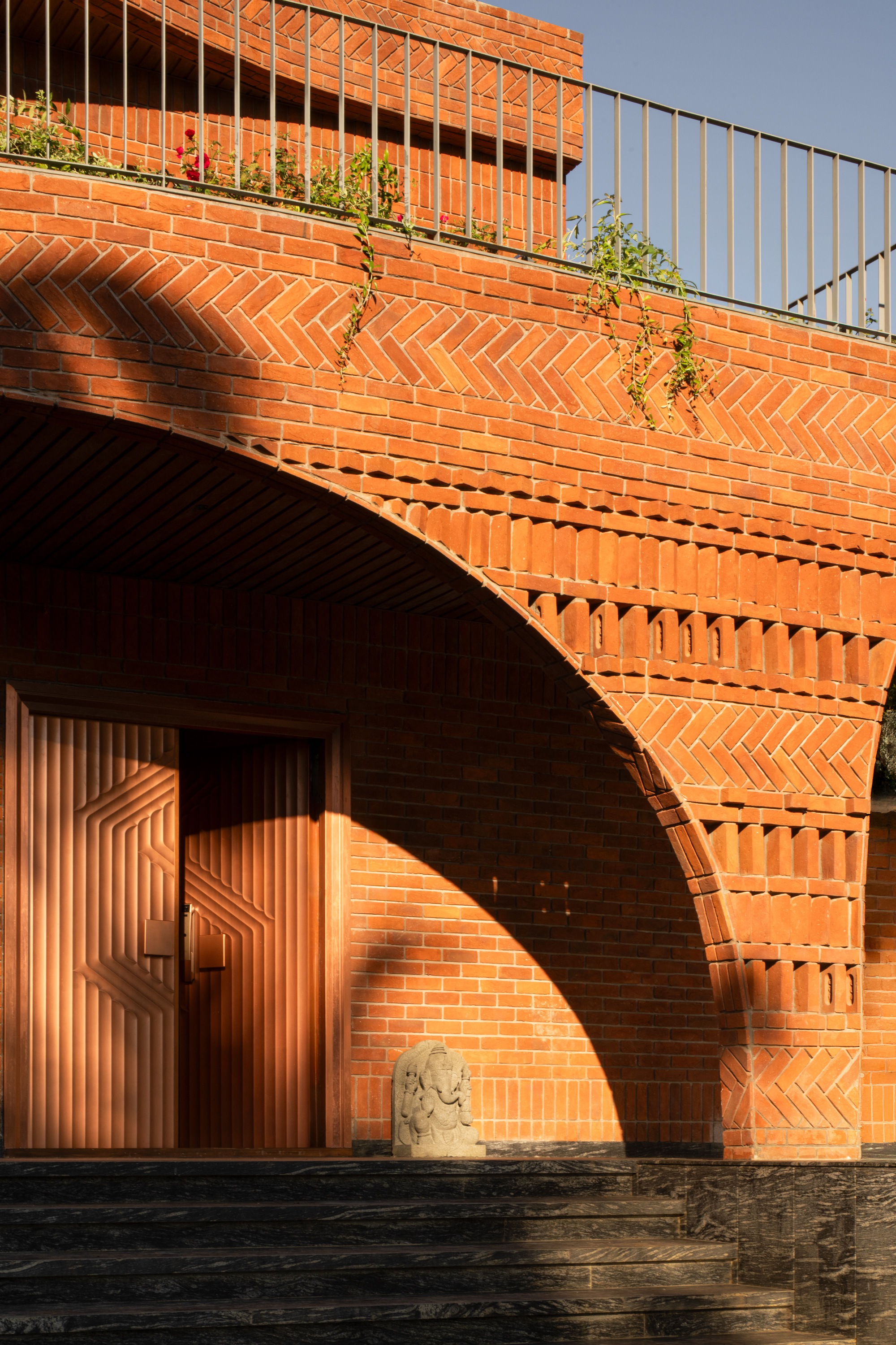 Arched brick entry with patterned brickwork, timber door and planted terrace under afternoon light