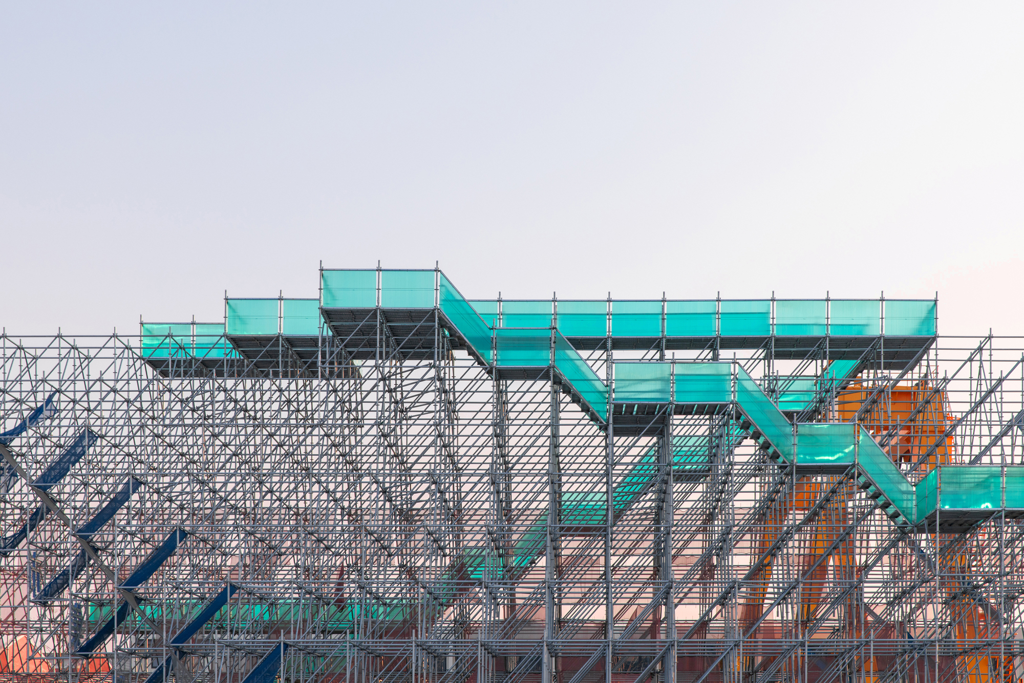 Detail of the turquoise stair platforms supported by the lattice of metal scaffolding tubes