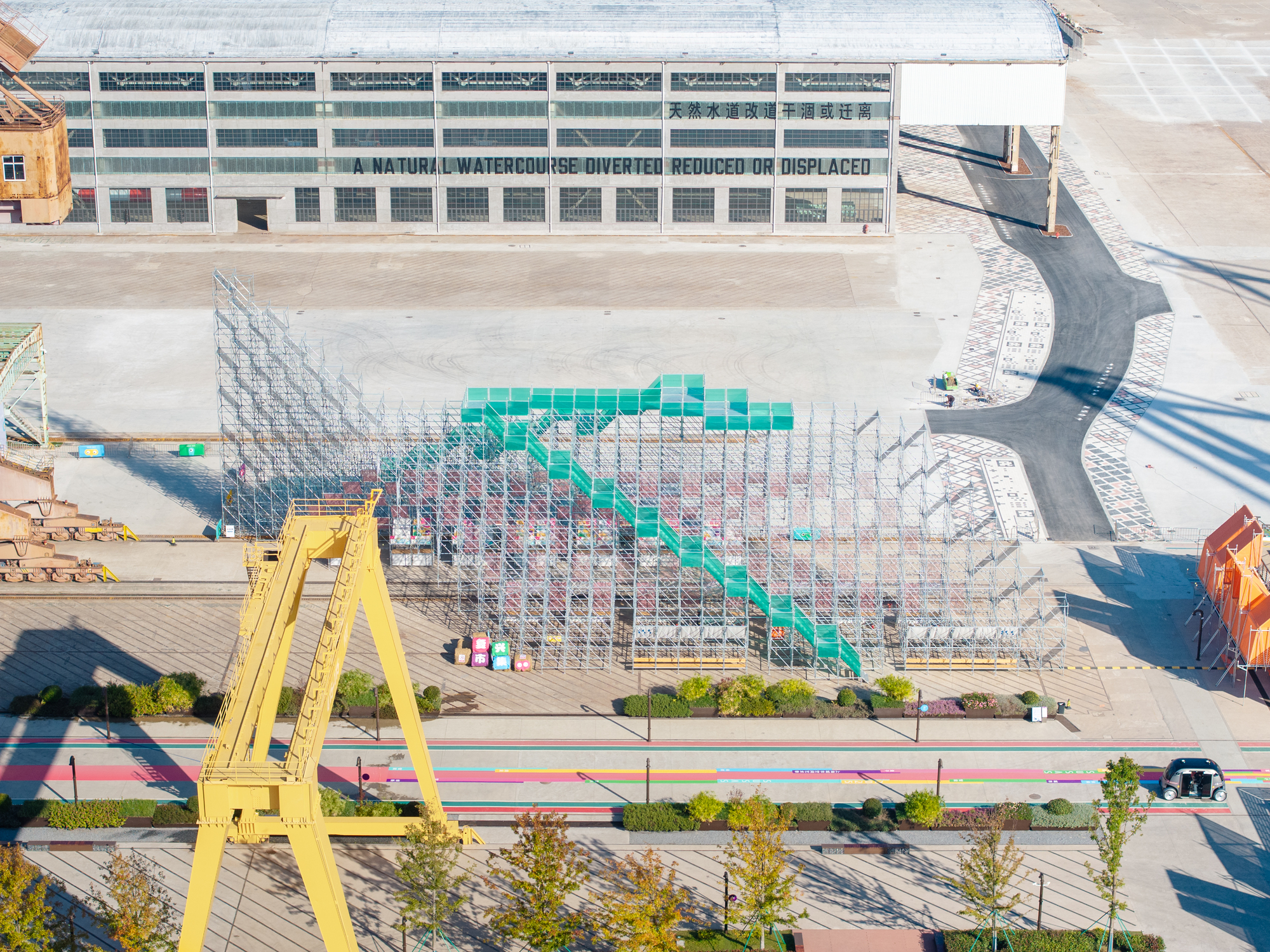Aerial view showing the triangular metal framework with colored infill panels on the waterfront plaza