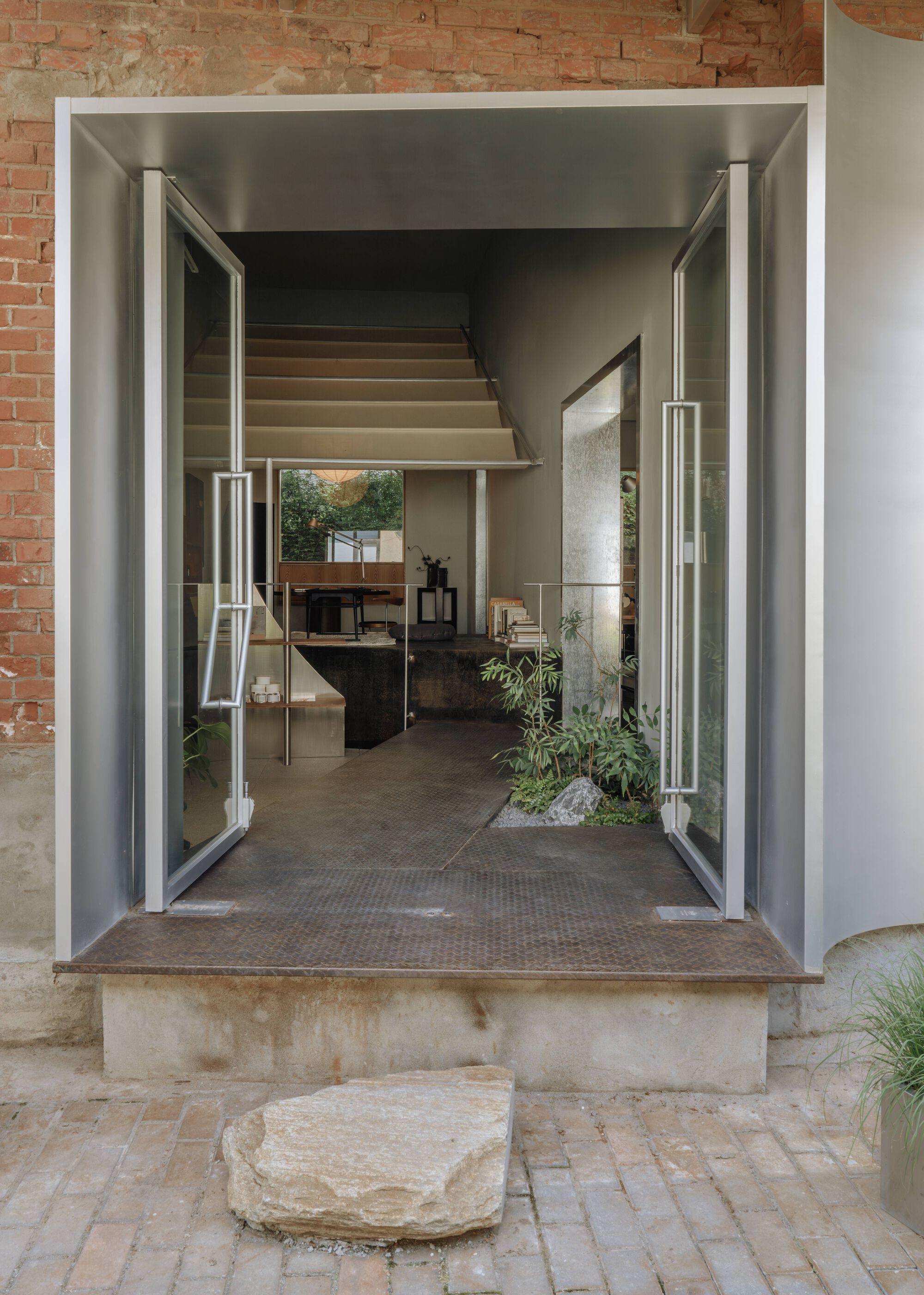 Open steel-framed pivot doors revealing an interior with raised platform and exposed brick walls beyond
